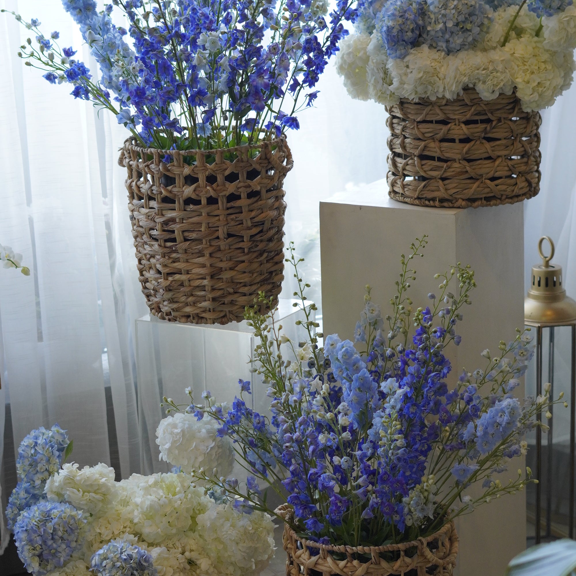 A matching set of four white and blue hydrangea basket arrangements featuring blue delphinium, styled for wedding ceremony decor by Moon's Flowers.