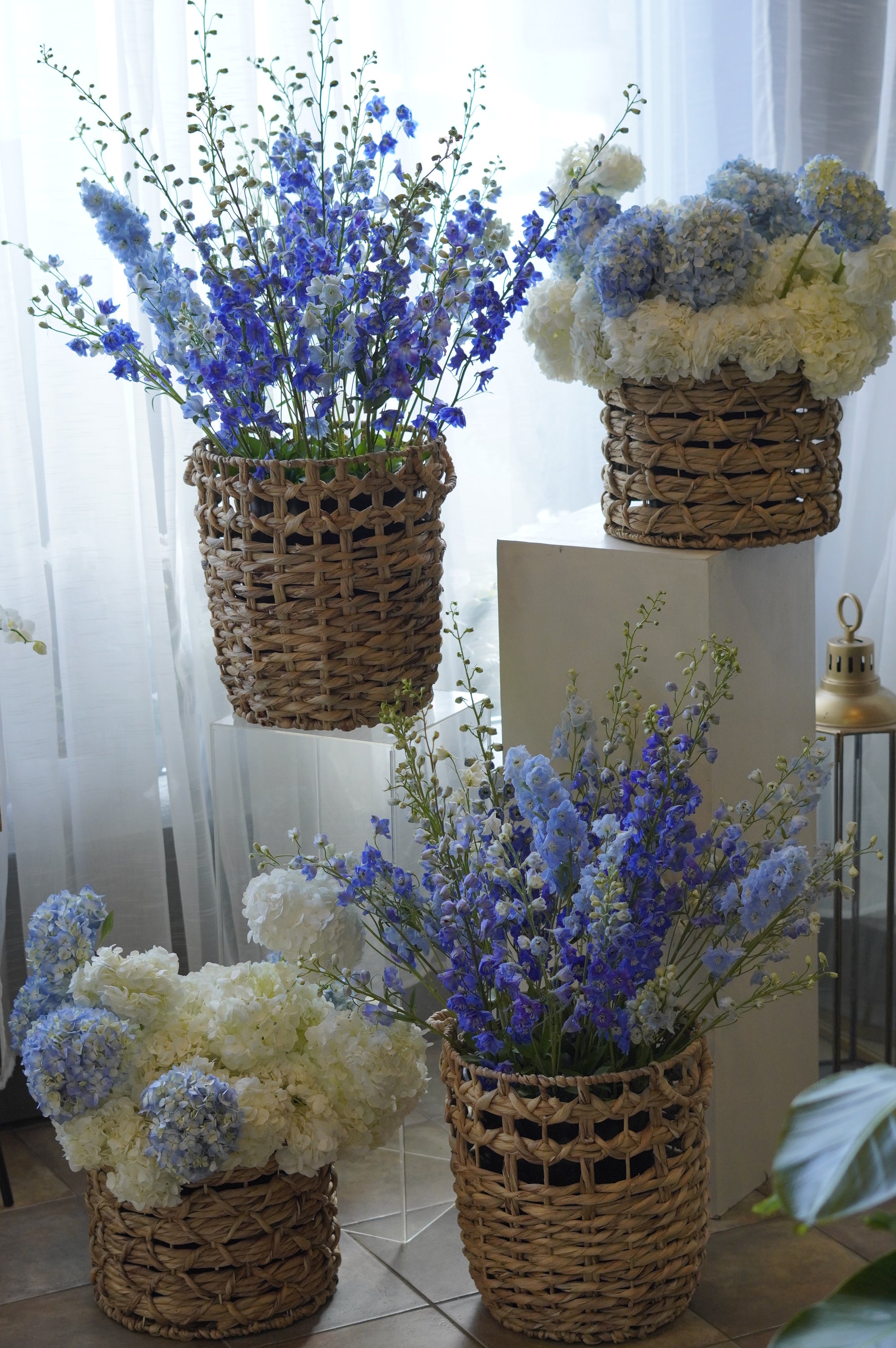 A matching set of four white and blue hydrangea basket arrangements featuring blue delphinium, styled for wedding ceremony decor by Moon's Flowers.
