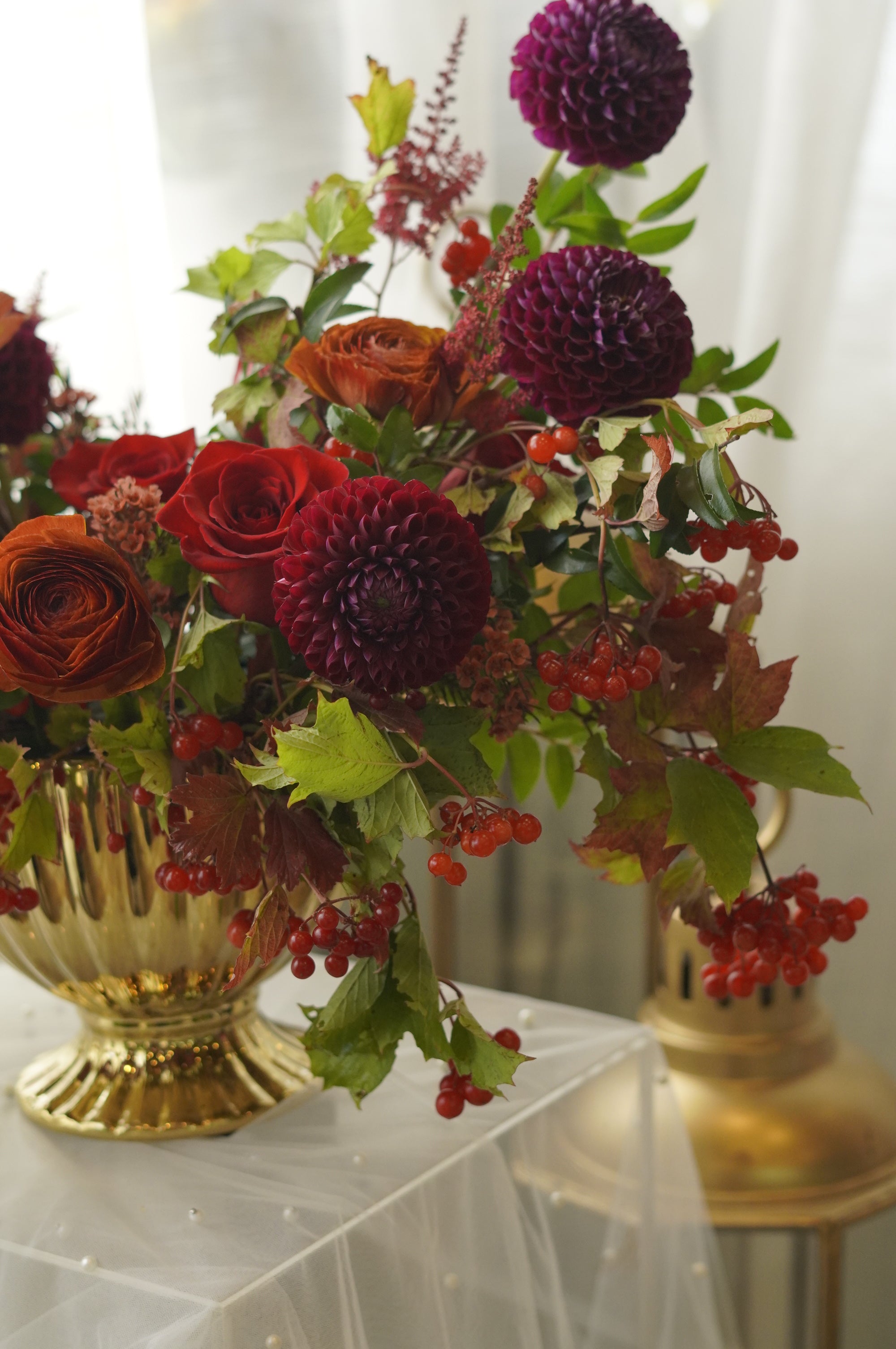 Close-up of burgundy flowers, red berries, and textured greenery in a gold urn