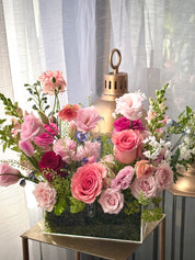Floral arrangement in a decorative box with pink and white flowers on a table.