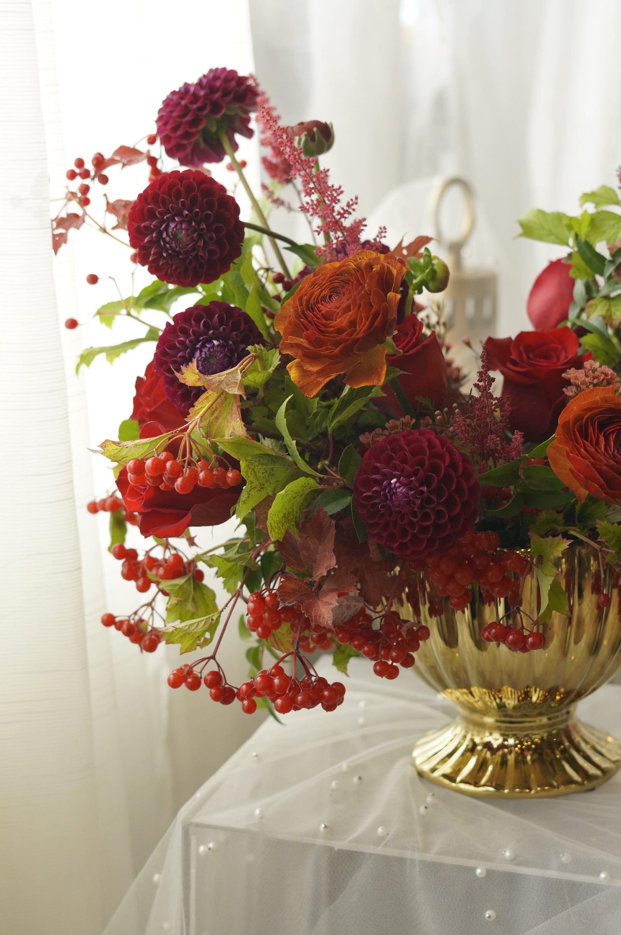 Red roses, orange roses, burgundy dahlia-style flowers, and autumn berries