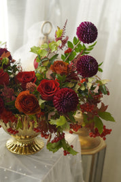 Wide view of ruby red and amber autumn flower arrangement in a gold urn