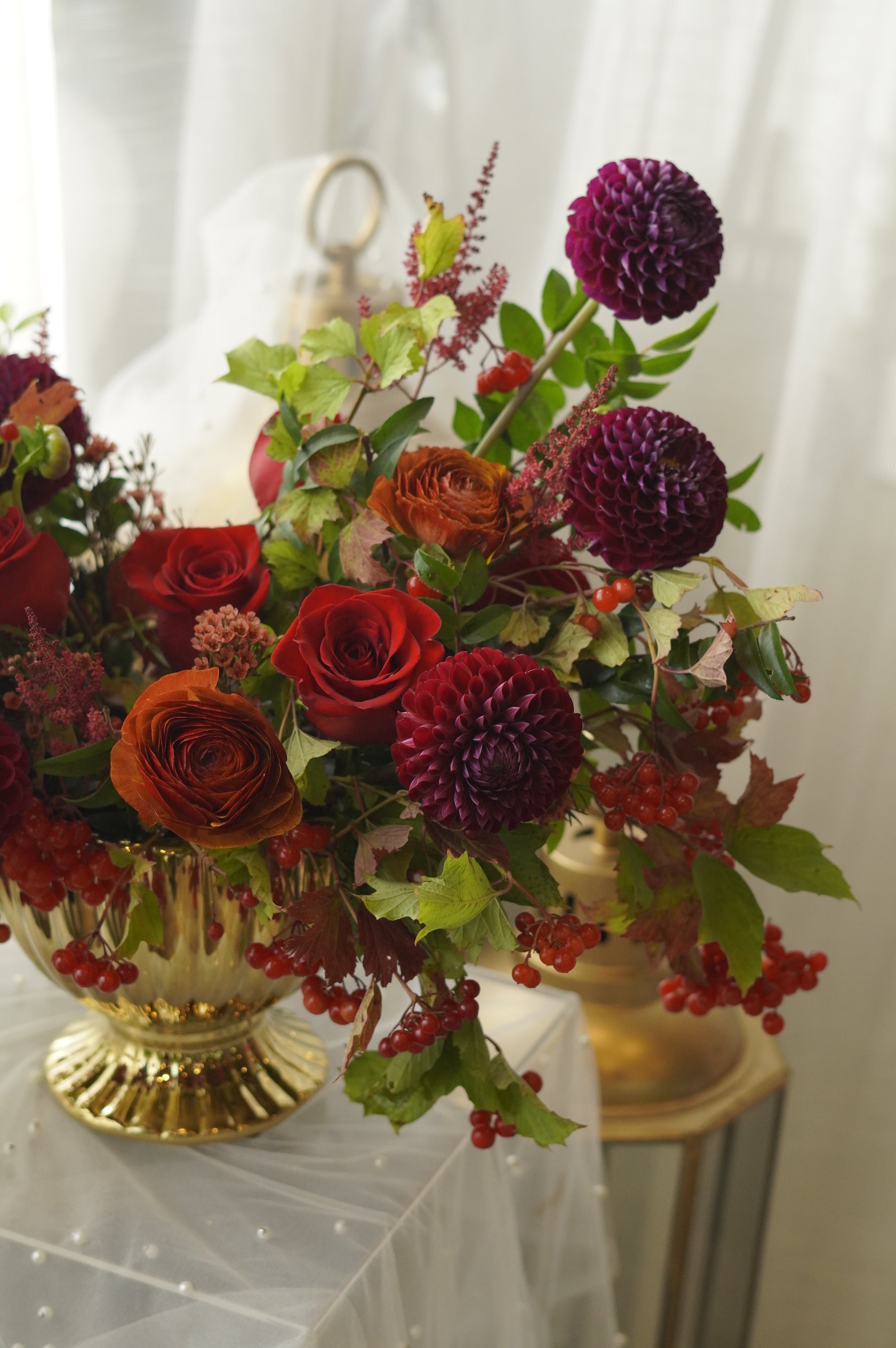 Wide view of ruby red and amber autumn flower arrangement in a gold urn
