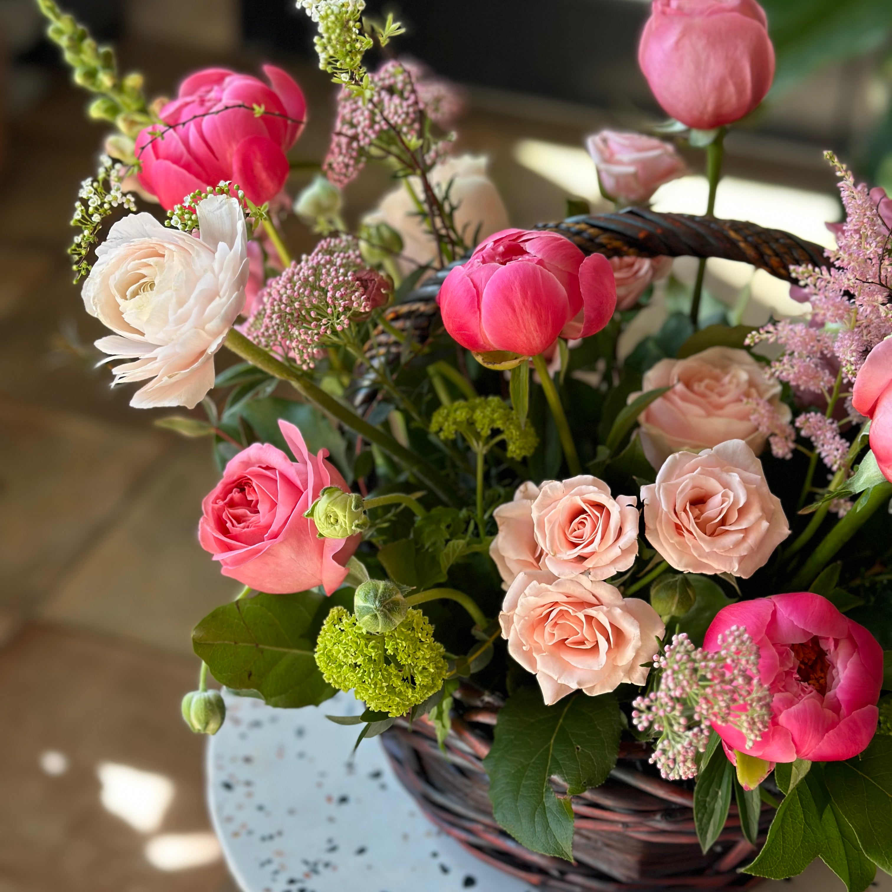 A close-up side view of the Mother's Day flower basket featuring pink peonies, garden roses, and delicate white blossoms in a dark wicker basket. Beautifully arranged seasonal flowers by Moon's Flowers Toronto