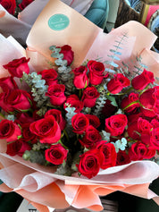 A lush Mother's Day bouquet of deep red roses accented with fresh silver dollar eucalyptus. The arrangement is wrapped in layered soft pink and peach premium paper, creating a romantic and vibrant gift by Moon's Flowers Toronto