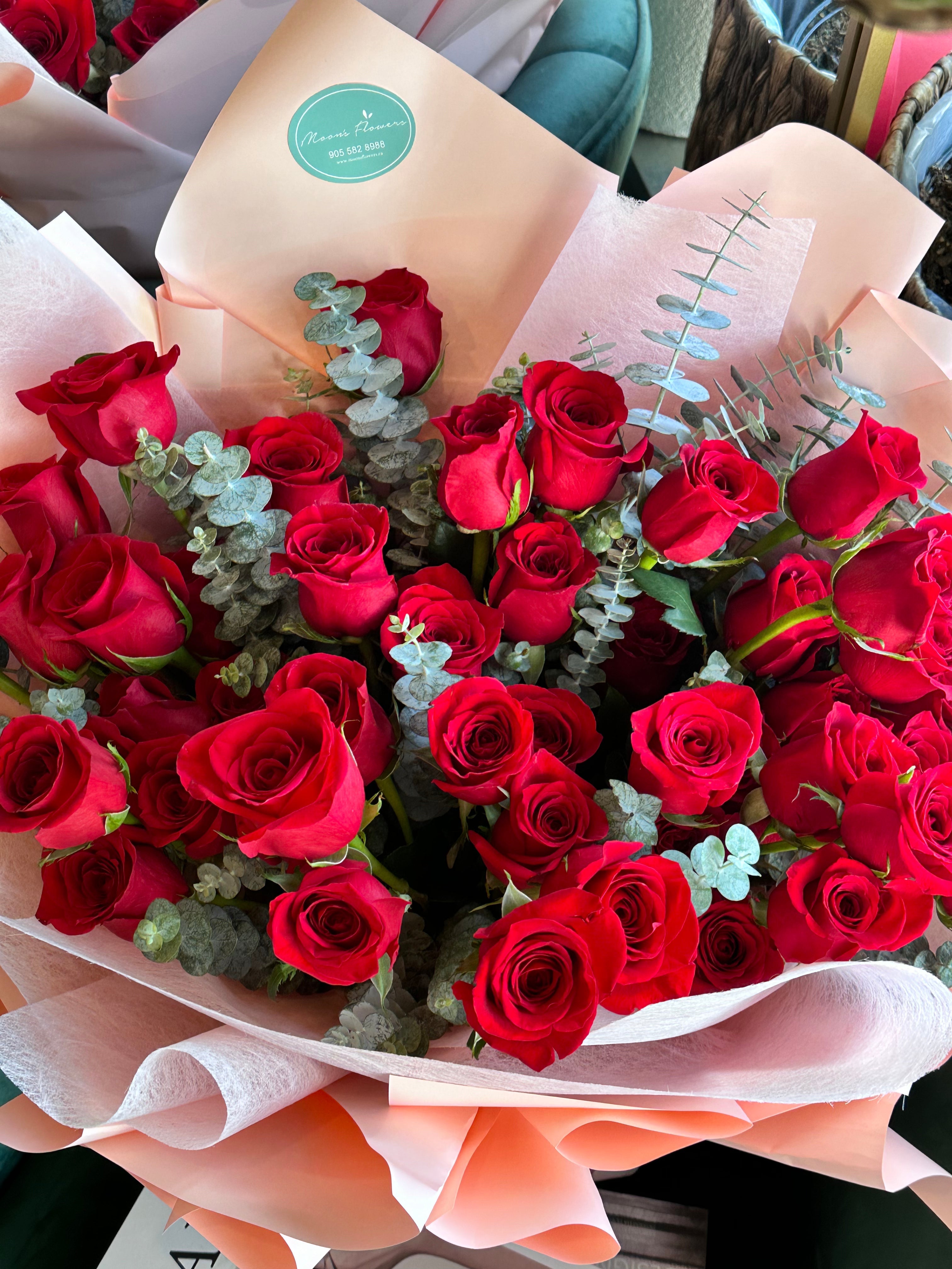 A lush Mother's Day bouquet of deep red roses accented with fresh silver dollar eucalyptus. The arrangement is wrapped in layered soft pink and peach premium paper, creating a romantic and vibrant gift by Moon's Flowers Toronto