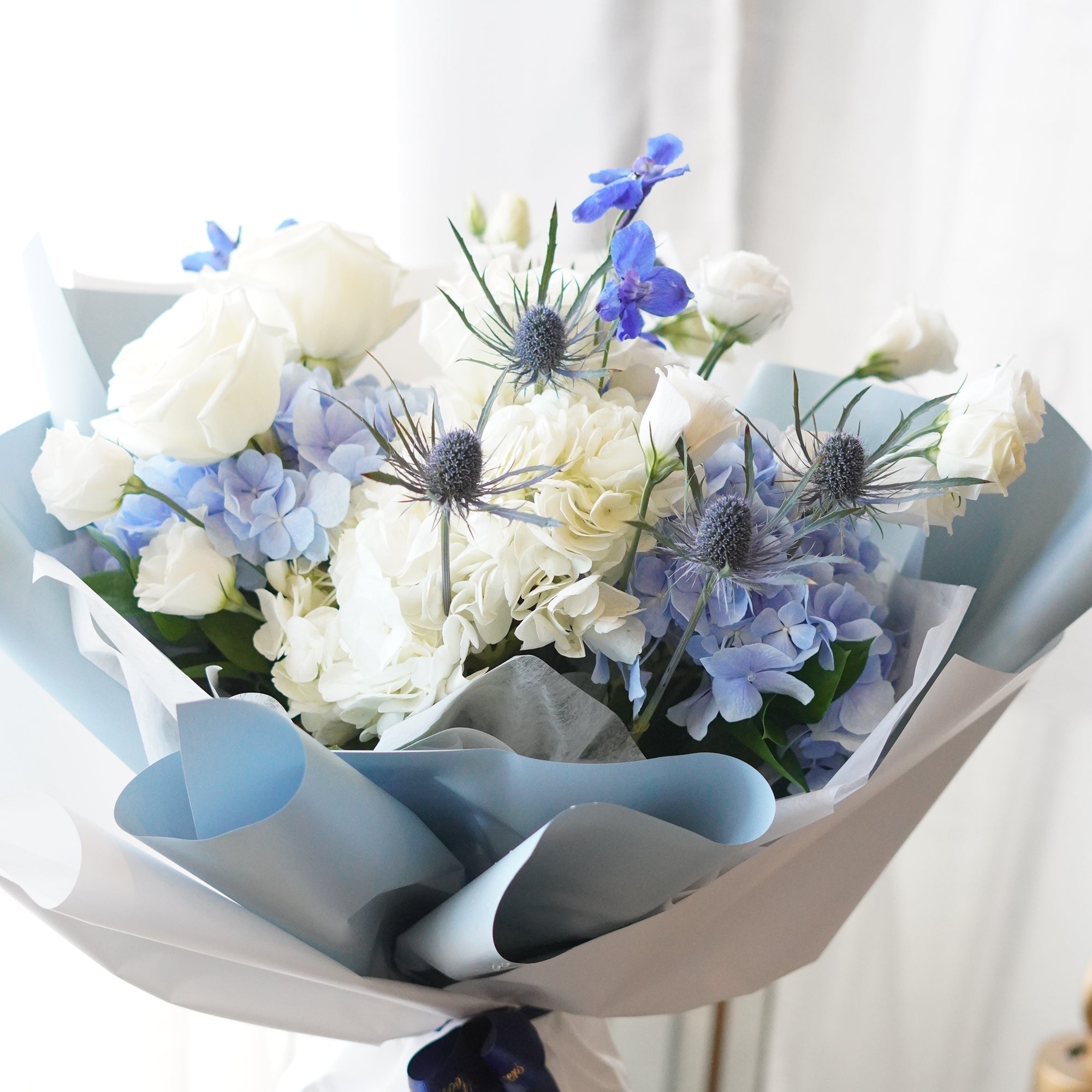 A lush bouquet of white and light blue hydrangeas, white roses, and purple-tipped lisianthus in a clear glass vase
