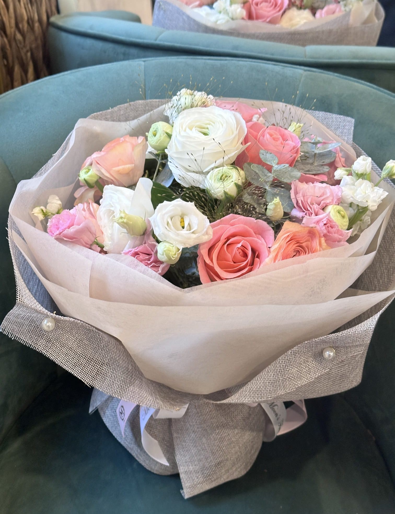 A luxurious Mother's Day flower bouquet featuring soft pink and peach roses, white lisianthus, and fresh eucalyptus leaves, elegantly wrapped in cream and grey textured paper
