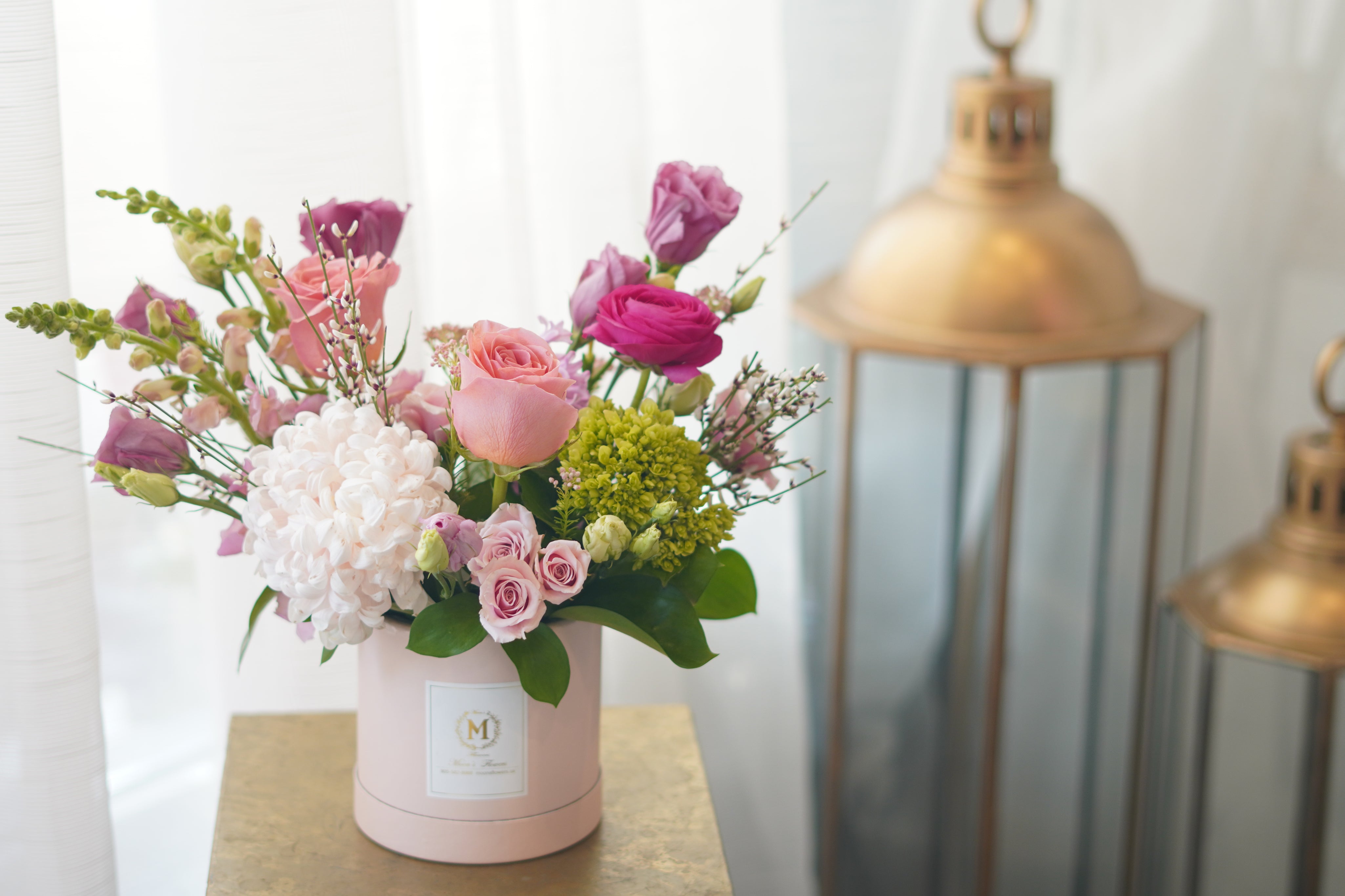 A modern floral arrangement in a gift box , featuring light pink roses, vibrant pink blooms, fresh green hydrangeas and natural seasonal greenery 
