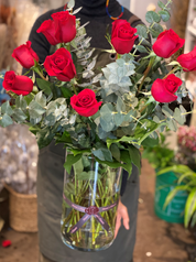 • A professional florist holding a Mother's Day bouquet of premium red roses and fresh eucalyptus in a clear glass vase.
• This hand-held view highlights the lush greenery and vibrant red petals, showcasing the high-quality floral design by Moon's Flowers Toronto.