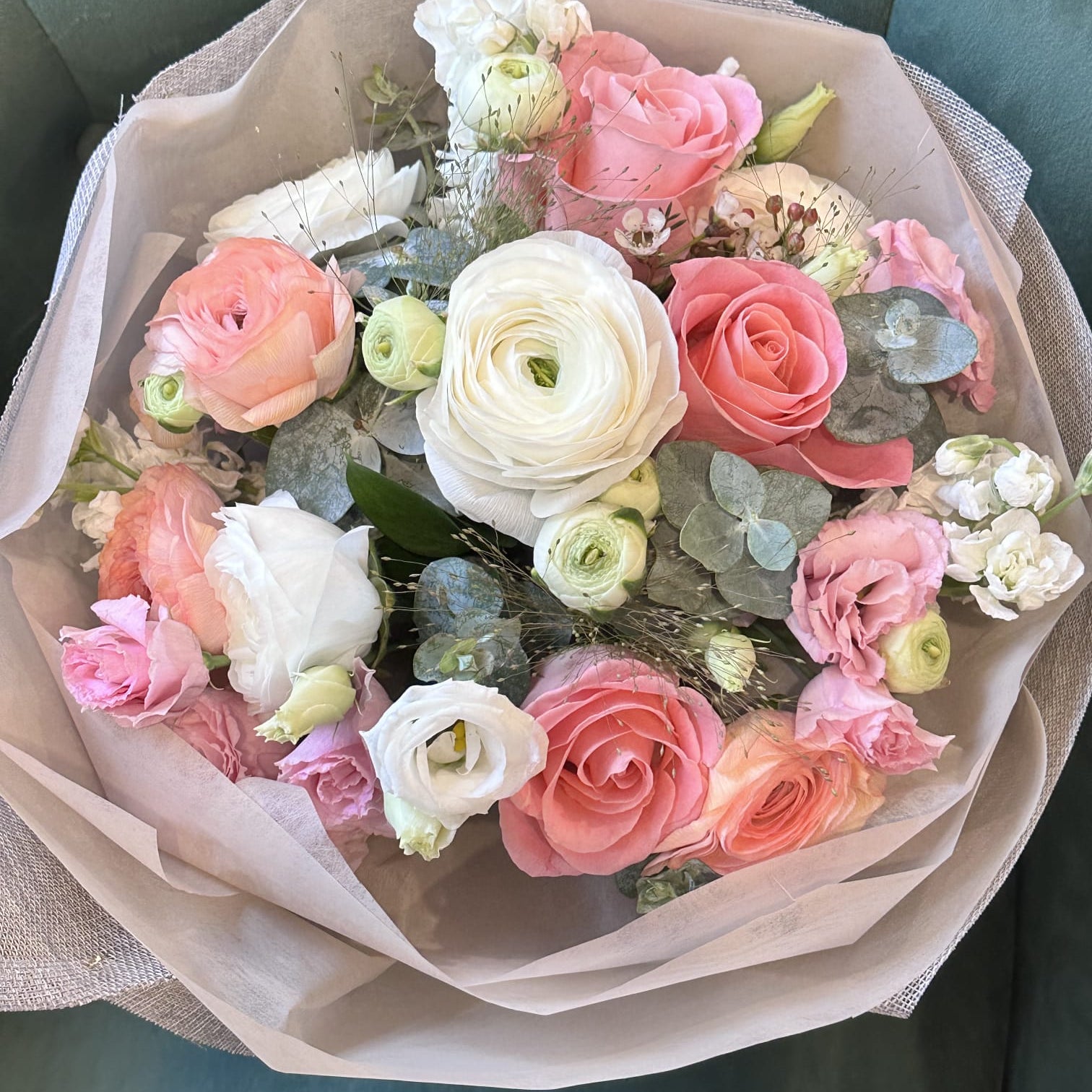 A romantic hand-tied bouquet of spring blooms and roses in soft peach and cream tones, wrapped in elegant neutral-toned fabric and paper