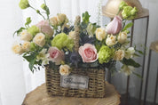 A rustic wicker flower basket filled with soft pink roses, creamy white roses, and textured green greenery. Moon's Flowers / Delivery in GTA