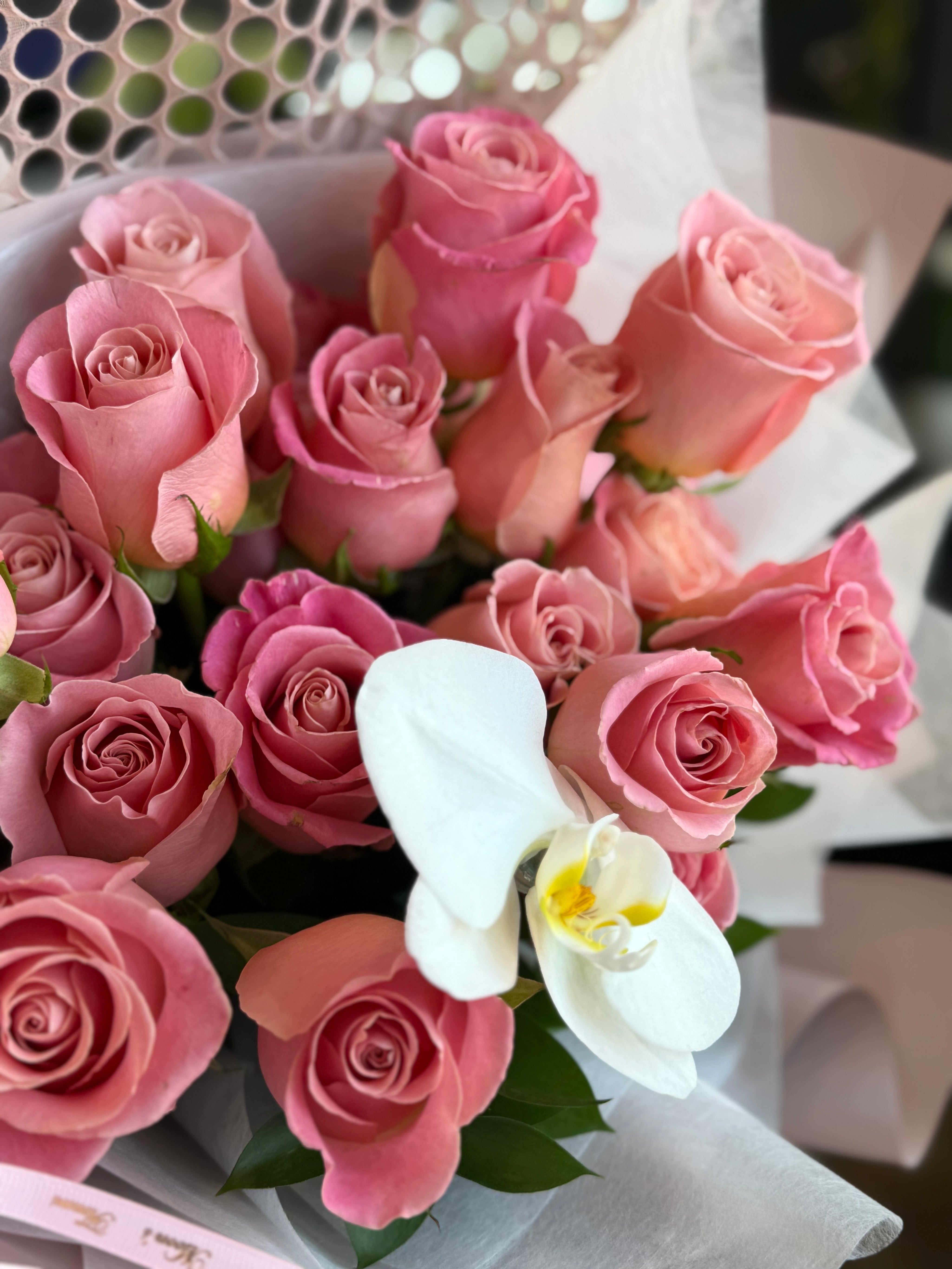 Blush pink rose bouquet with white orchid and fresh greenery in elegant wrapping