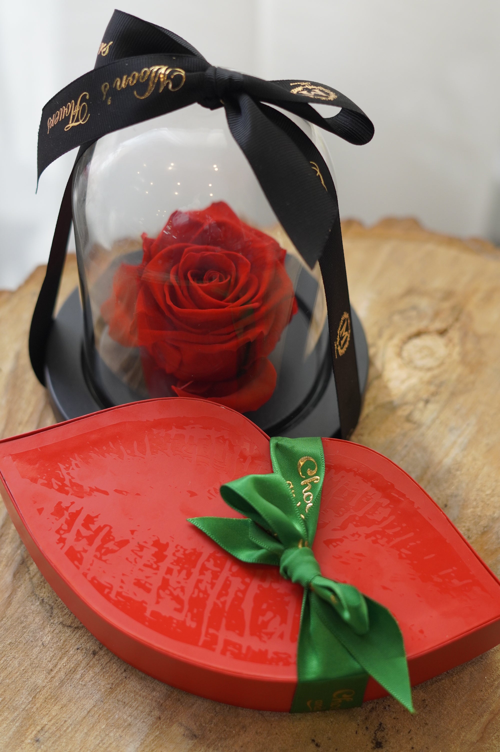Lip-shaped red gift box with a green ribbon and a preserved rose inside, on a wooden surface.