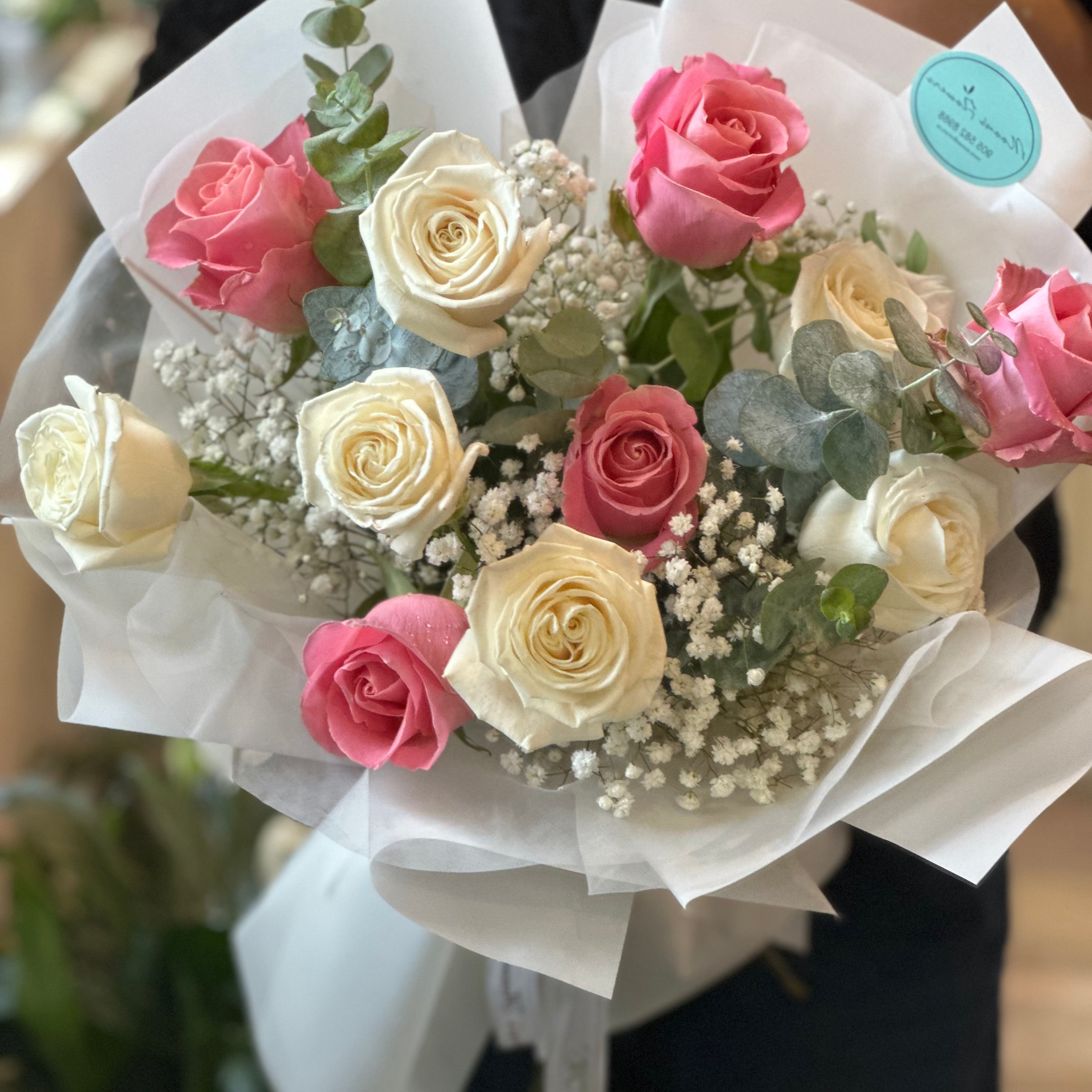 Person holding a classic pink and white rose dozen bouquet with greenery