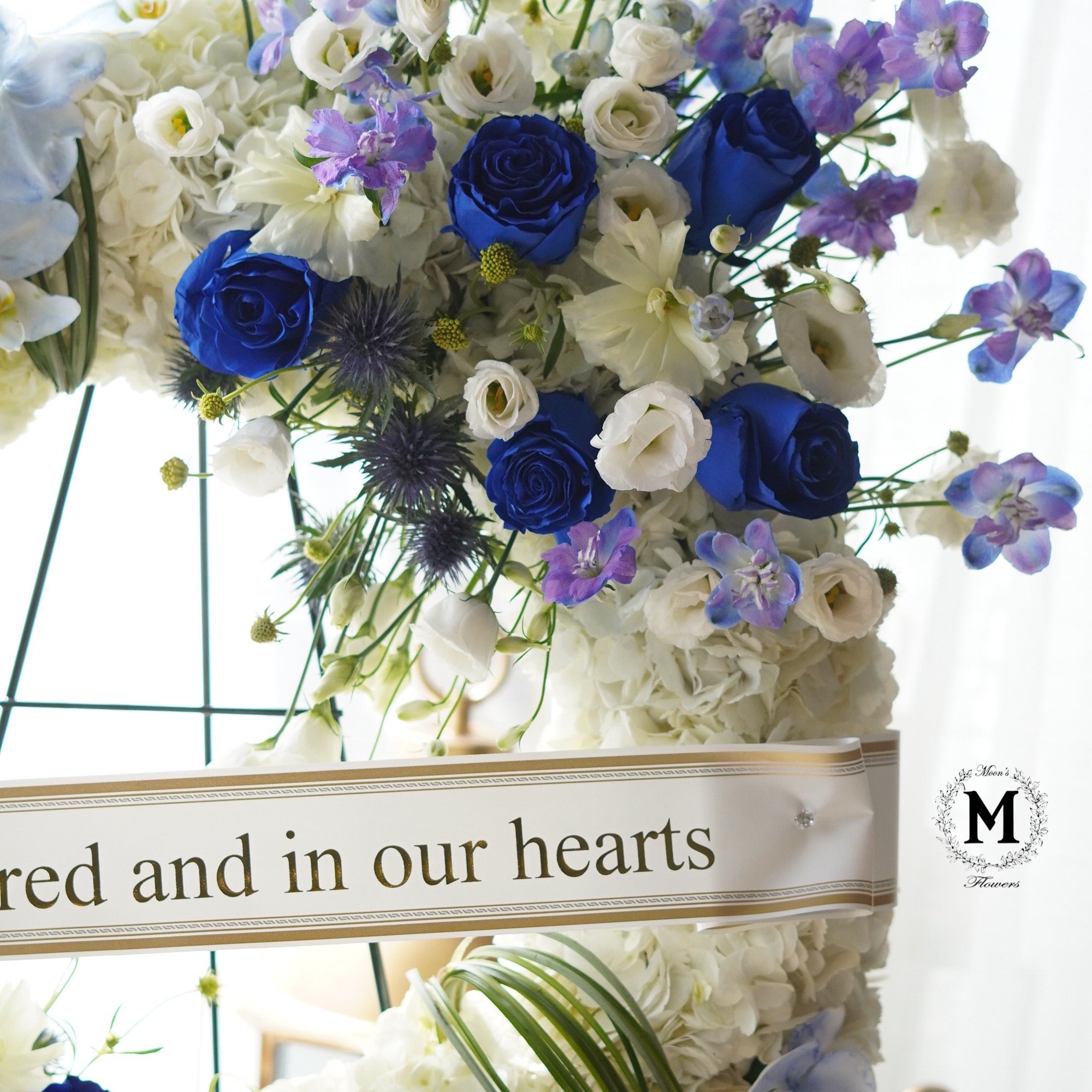 Close-up of premium blue roses and lavender blooms in a condolence wreath arrangement.