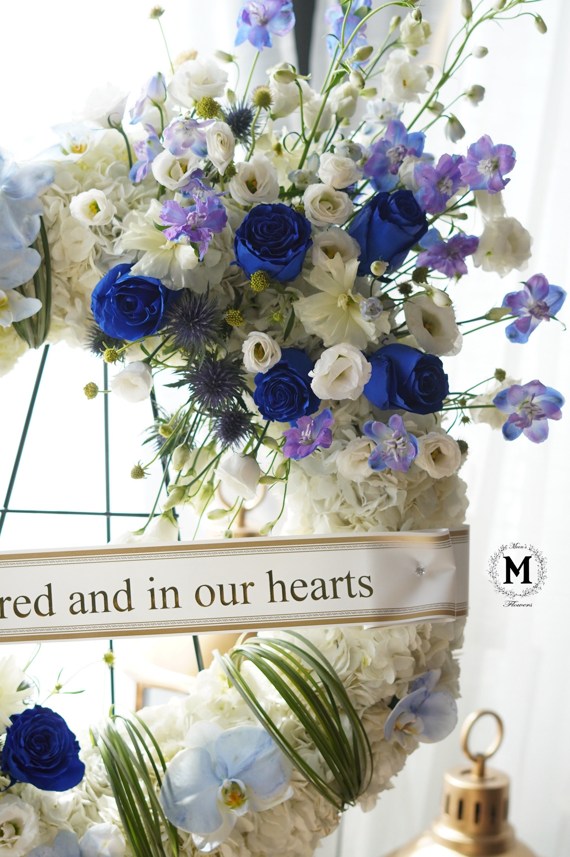 Close-up of premium blue roses and lavender blooms in a condolence wreath arrangement.