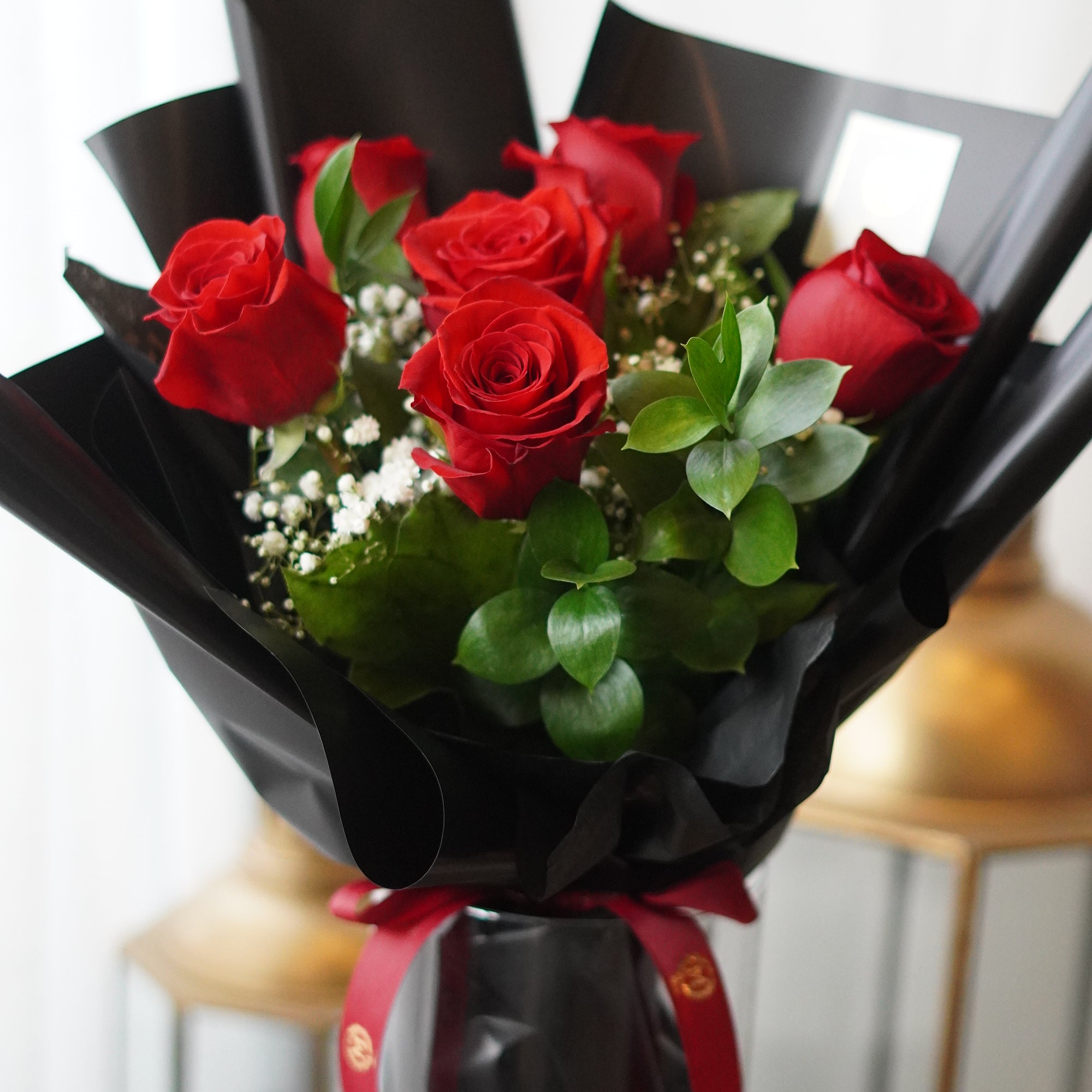 Half dozen red roses with baby’s breath wrapped in Moon’s Flowers’ signature packaging