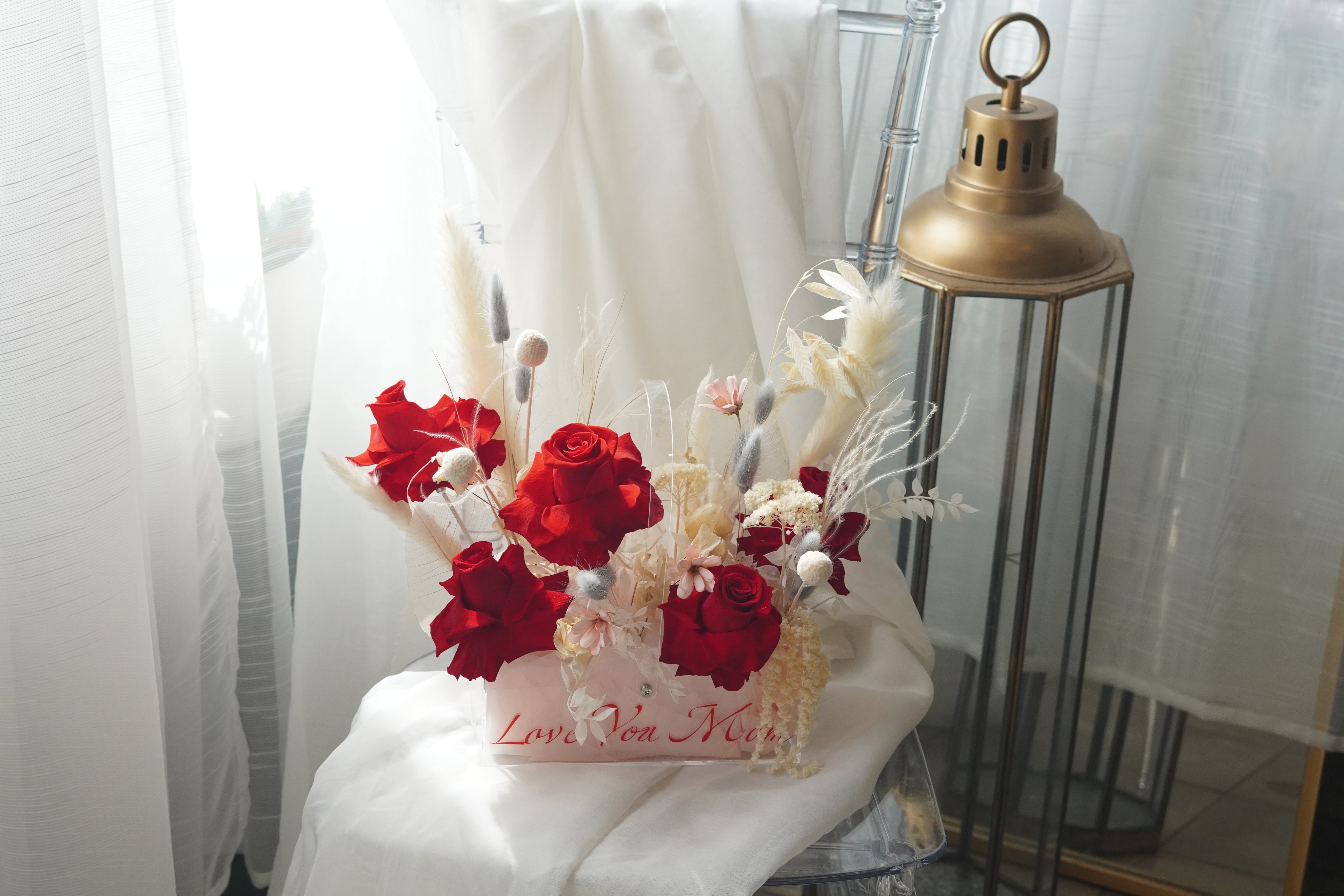 Preserved red rose arrangement with dried white florals in a transparent box featuring "Love You Mom" calligraphy.