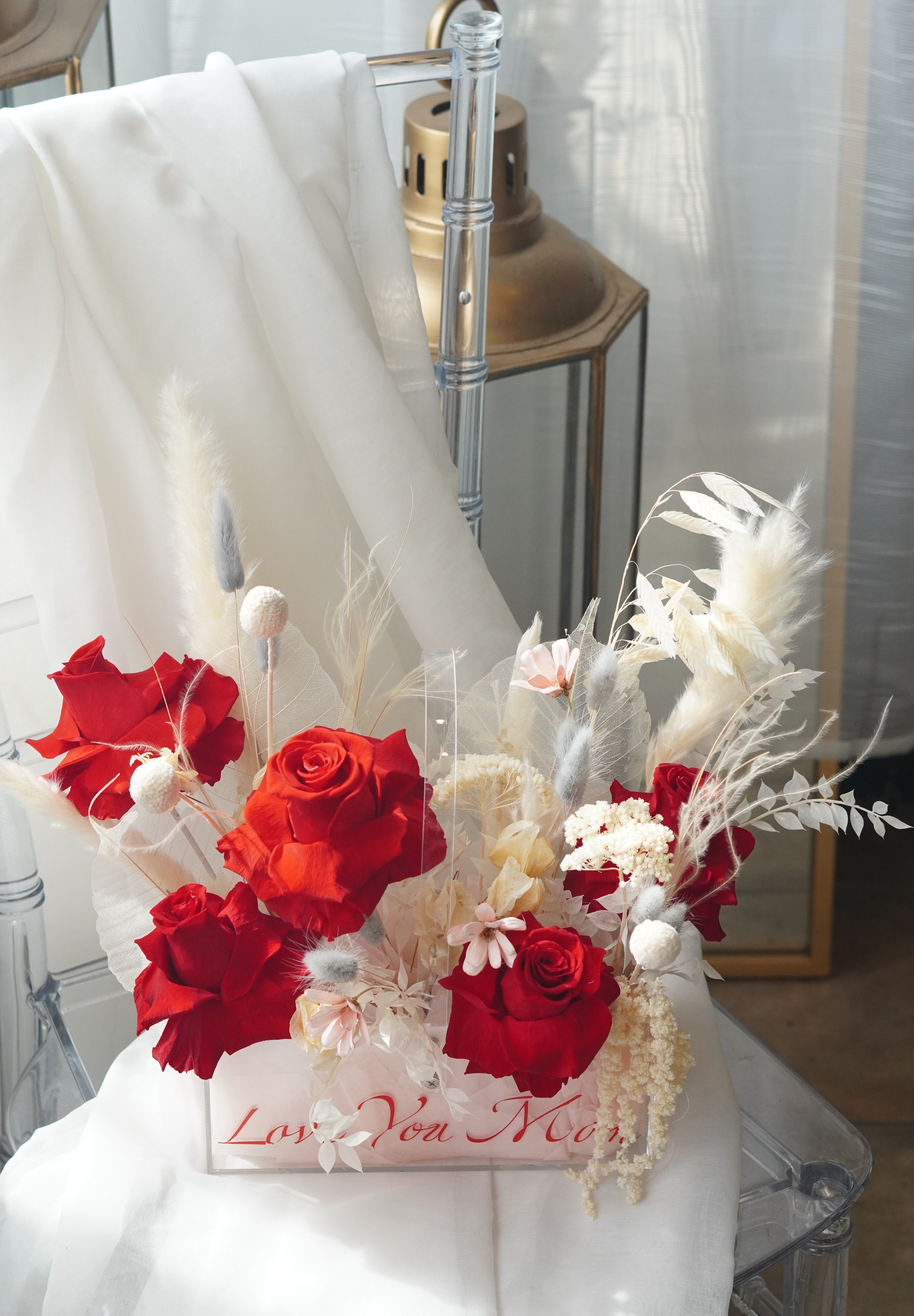 Preserved red rose arrangement with dried white florals in a transparent box featuring "Love You Mom" calligraphy.