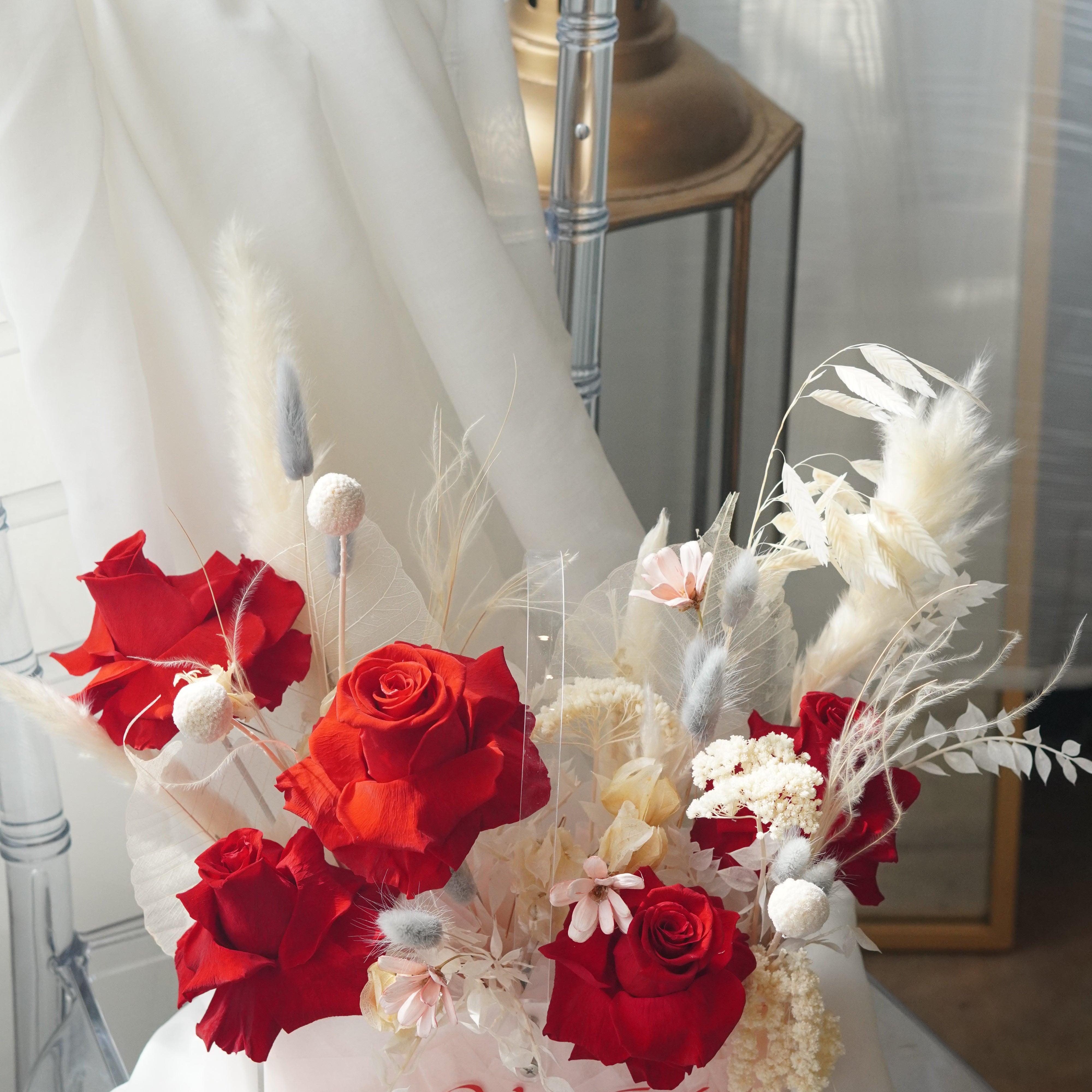 Red preserved roses and dried white flowers in a clear gift box.