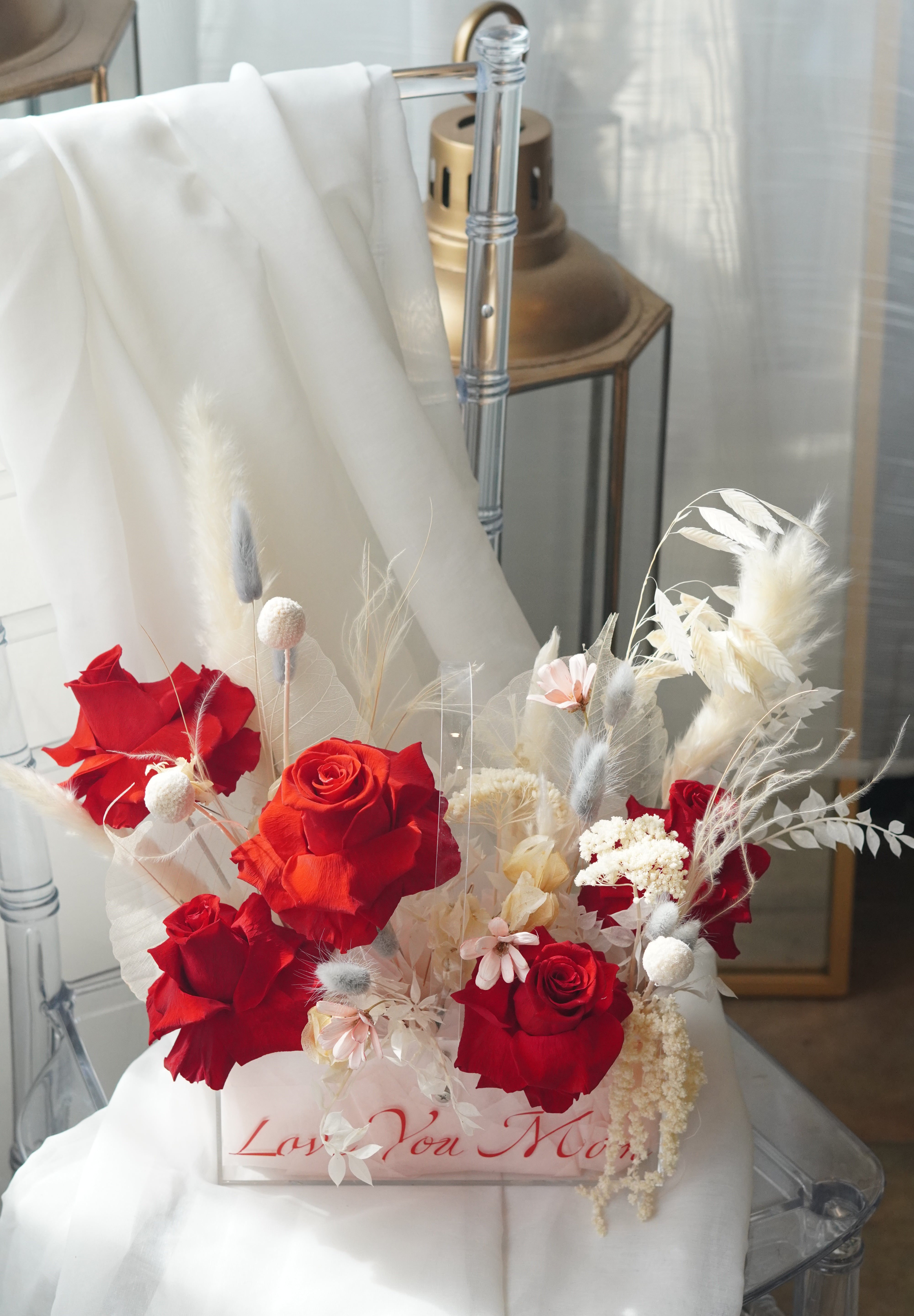 Red preserved roses and dried white flowers in a clear gift box.
