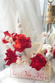 Preserved red rose arrangement with dried white florals in a transparent box featuring "Love You Mom" calligraphy.