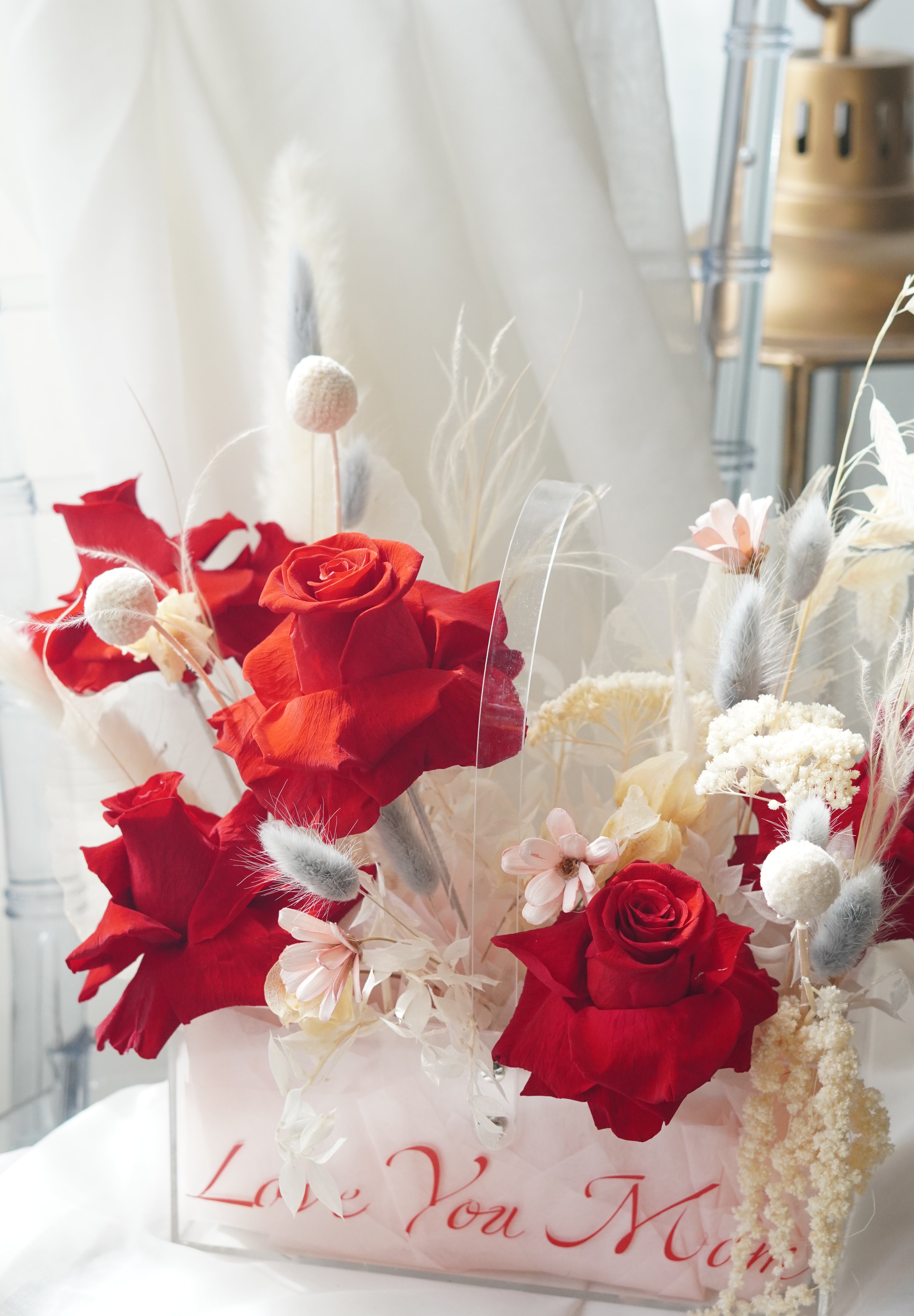 Preserved red rose arrangement with dried white florals in a transparent box featuring "Love You Mom" calligraphy.