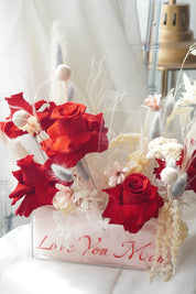 Luxury floral arrangement titled Velvet Love Bloom, featuring deep red preserved roses, white pampas grass, and neutral dried textures in a modern acrylic box.