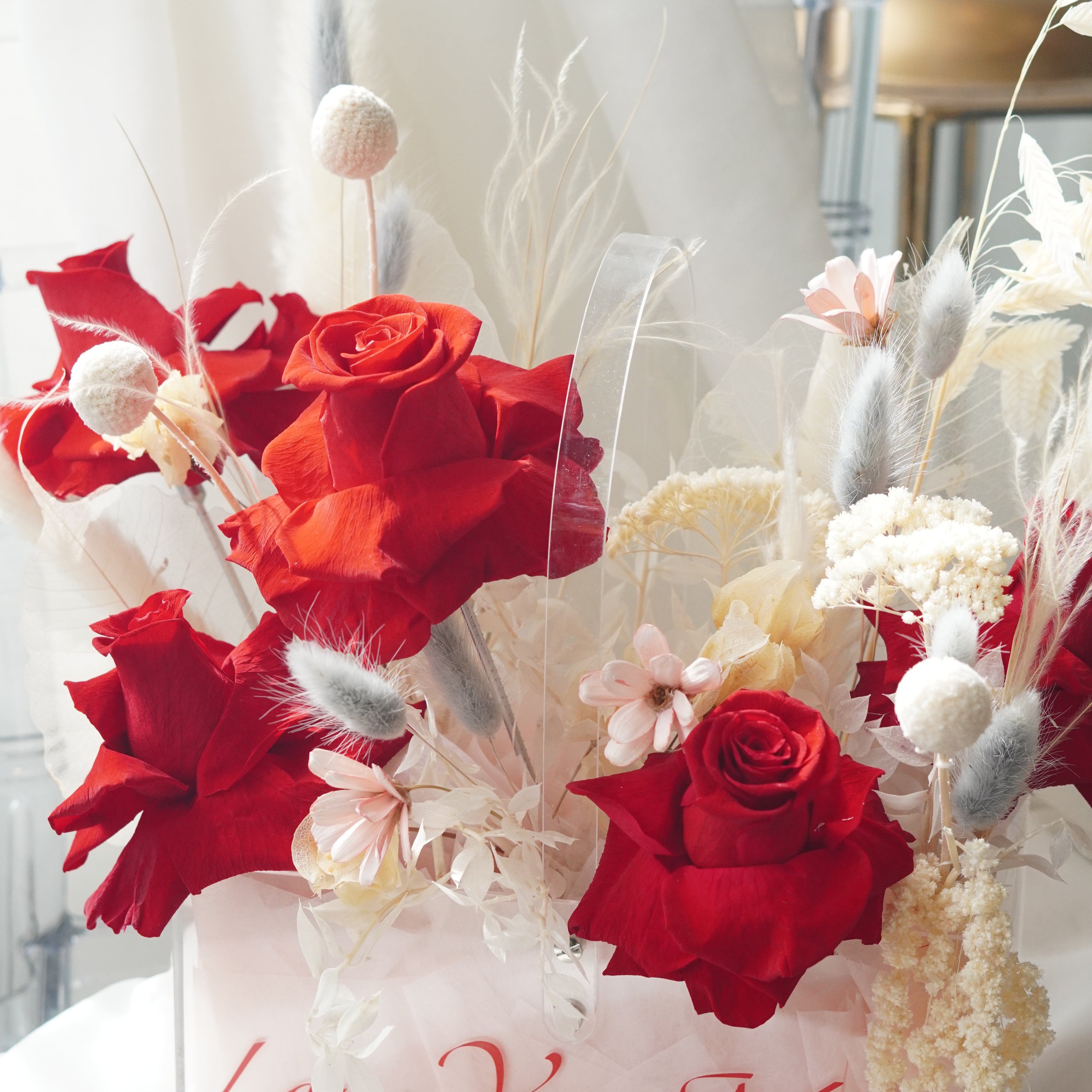 Luxury floral arrangement titled Velvet Love Bloom, featuring deep red preserved roses, white pampas grass, and neutral dried textures in a modern acrylic box.