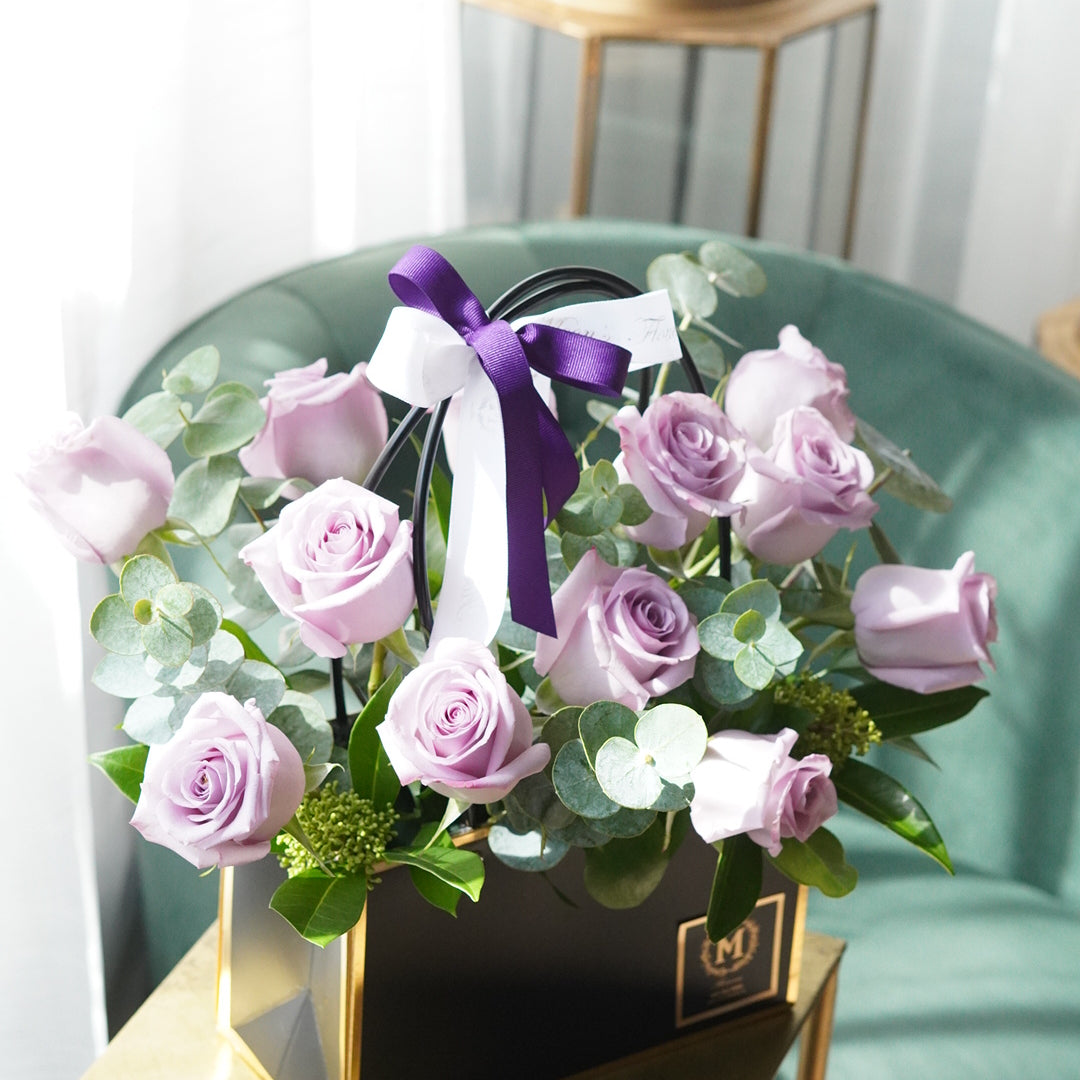 Dozen lavender roses arranged in a modern basket with purple and light purple roses