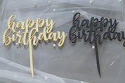  Gold and black "happy birthday" acrylic cake toppers laid on white tulle with pearl accents