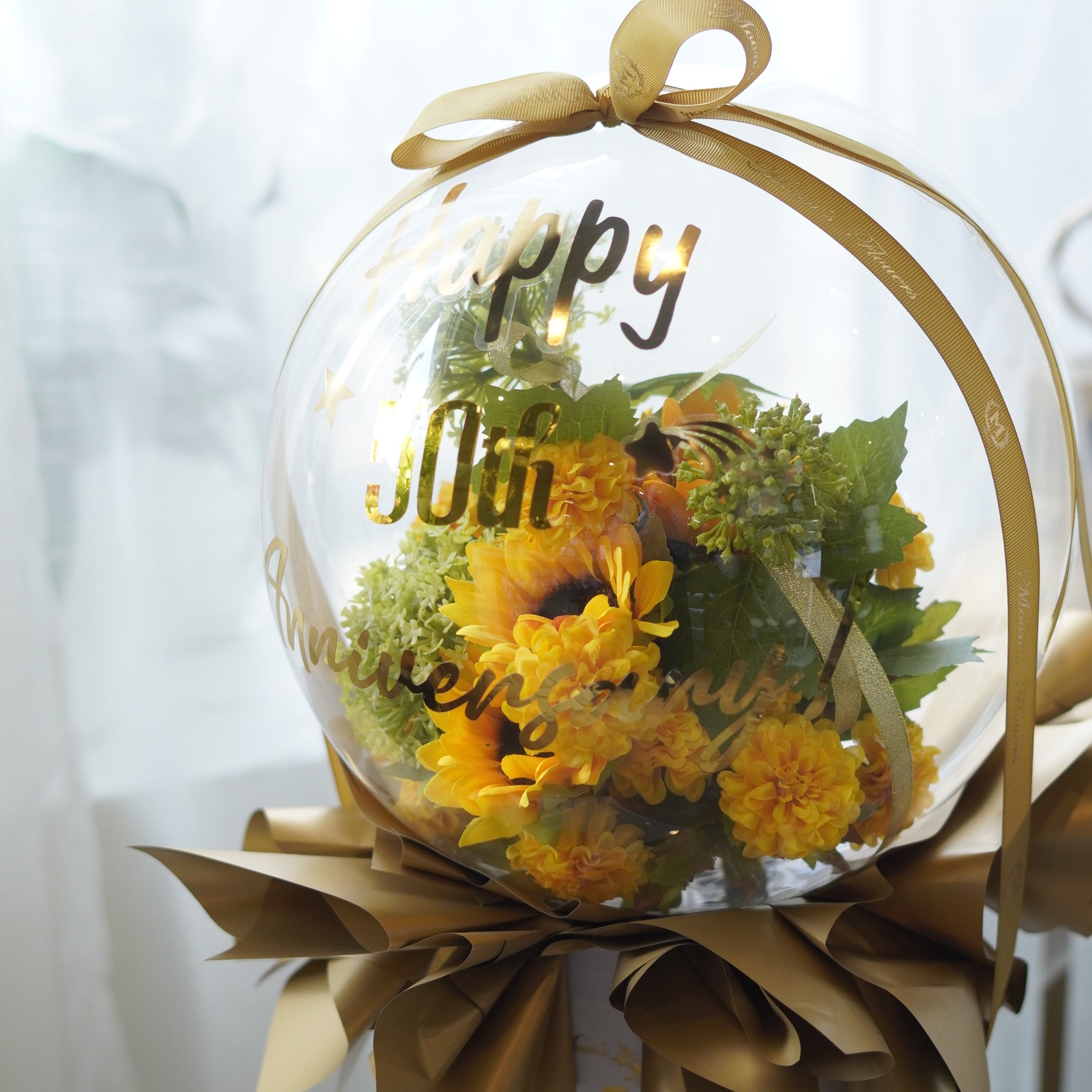 Artificial flower balloon arrangement with soft blush pink and peach flowers inside a clear display dome with tulle and ribbon