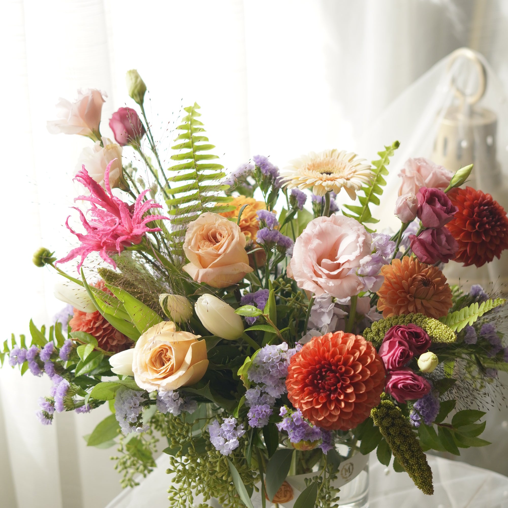 Orange, peach and lavender seasonal flower arrangement with textured greenery