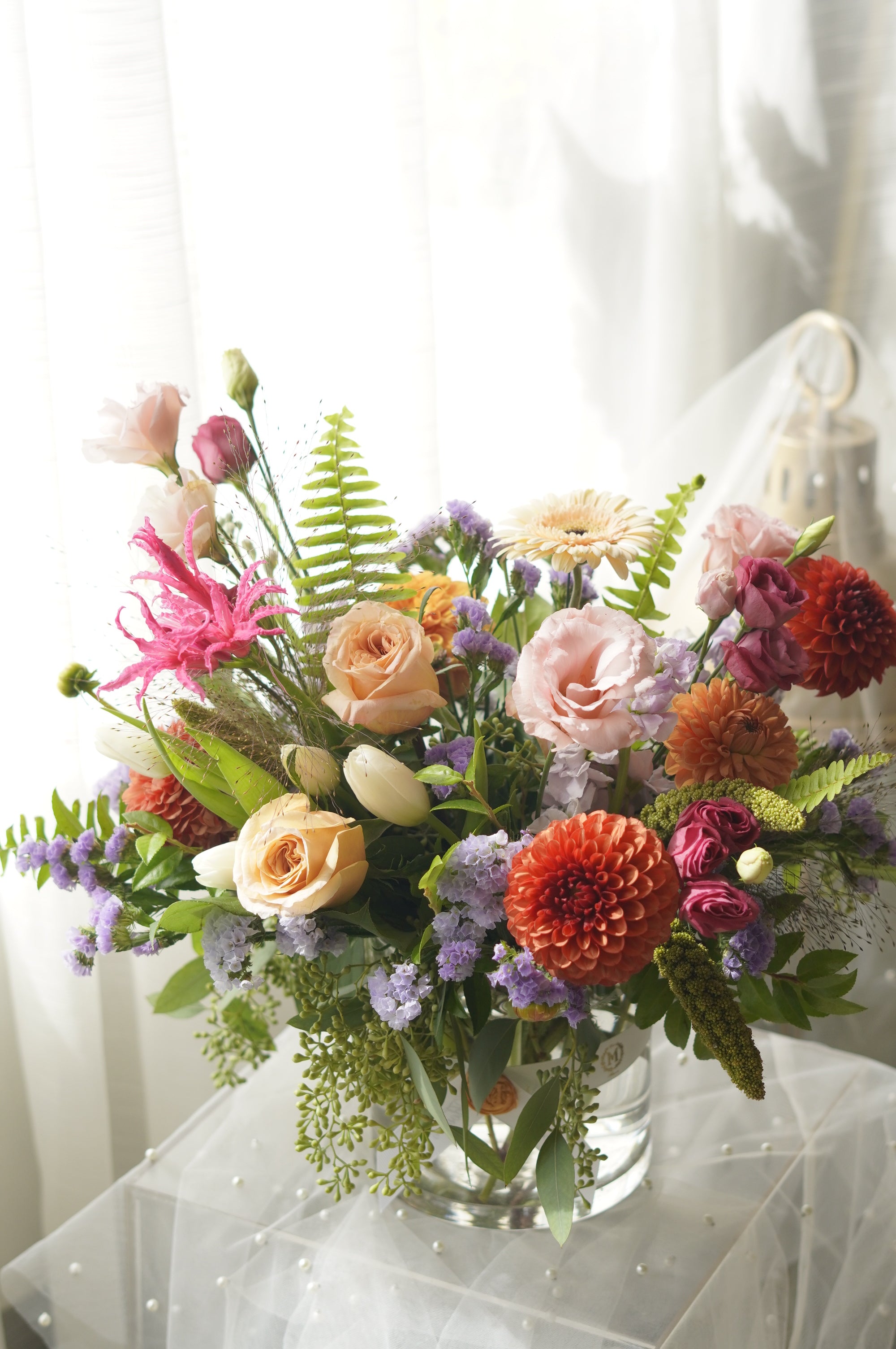 Orange, peach and lavender seasonal flower arrangement with textured greenery