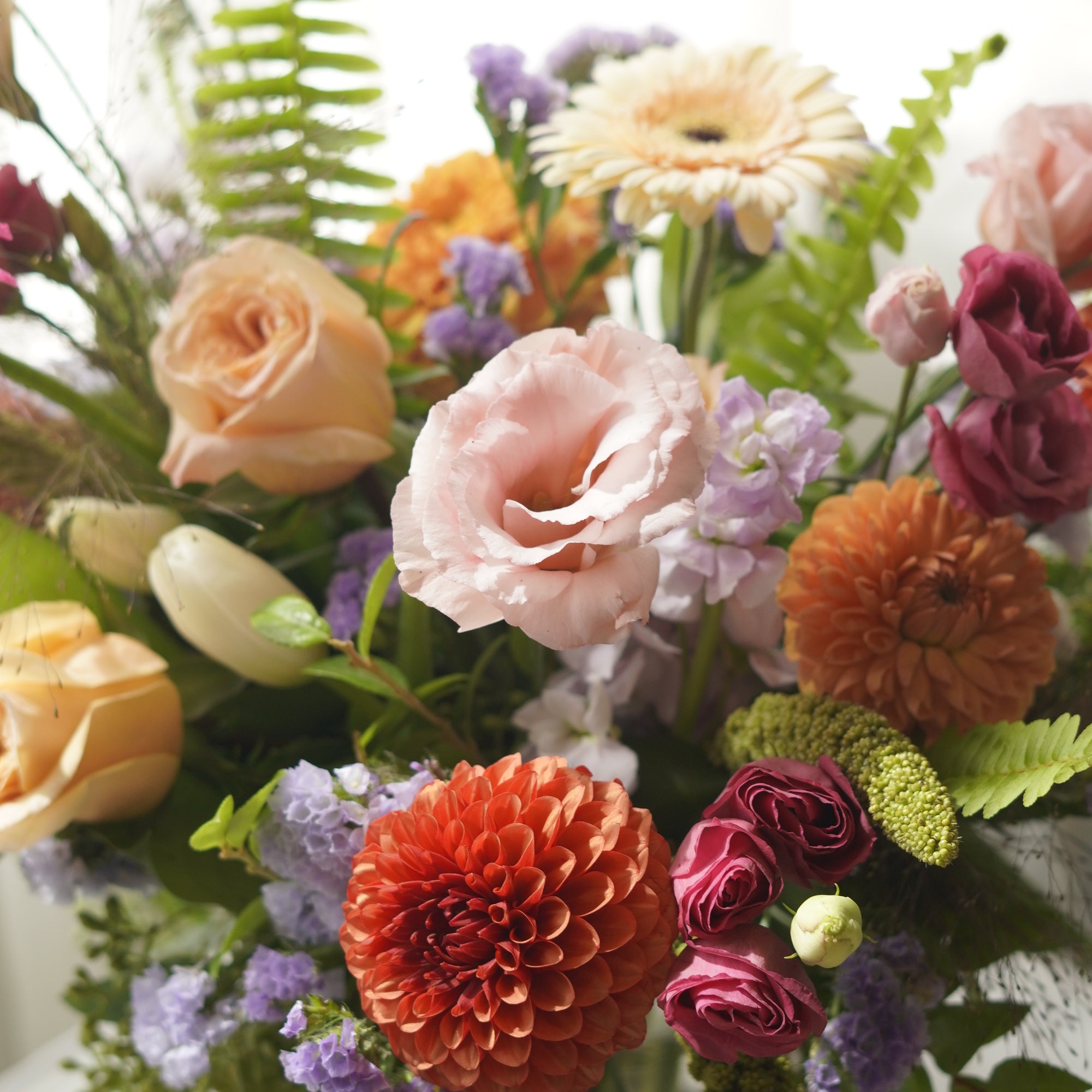 Close-up of orange dahlias, pink lisianthus and purple seasonal flowers in Tangerine arrangement