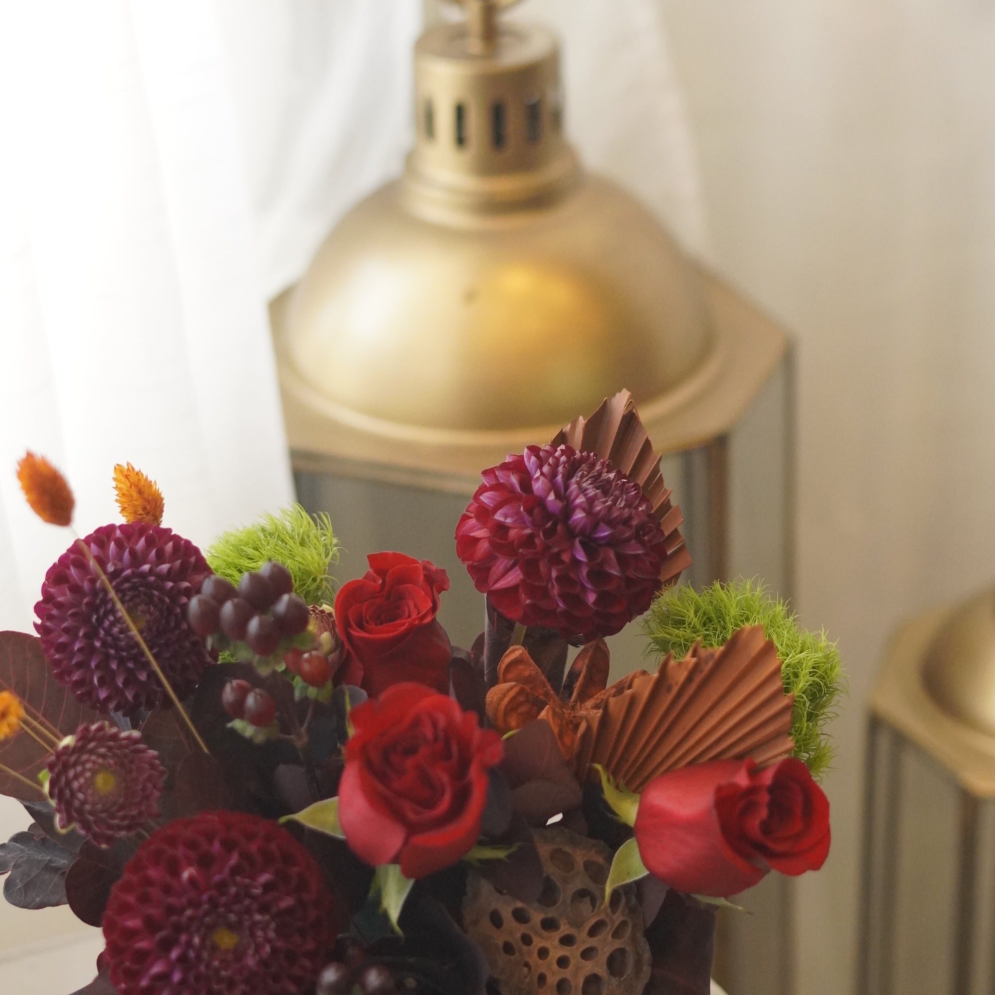 Red roses and burgundy dahlias with dried palm accents — autumn flower arrangement