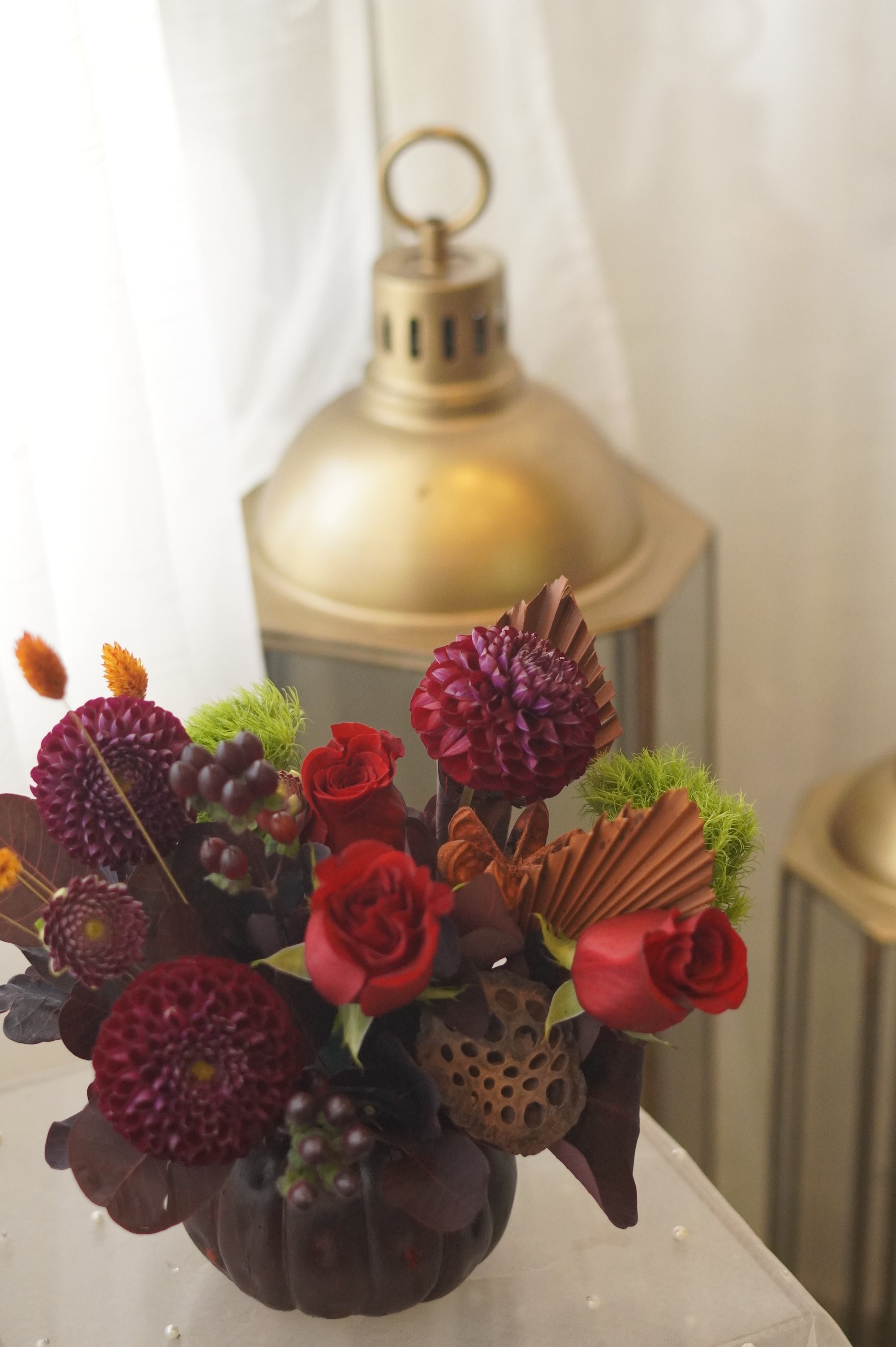 Red roses and burgundy dahlias with dried palm accents — autumn flower arrangement