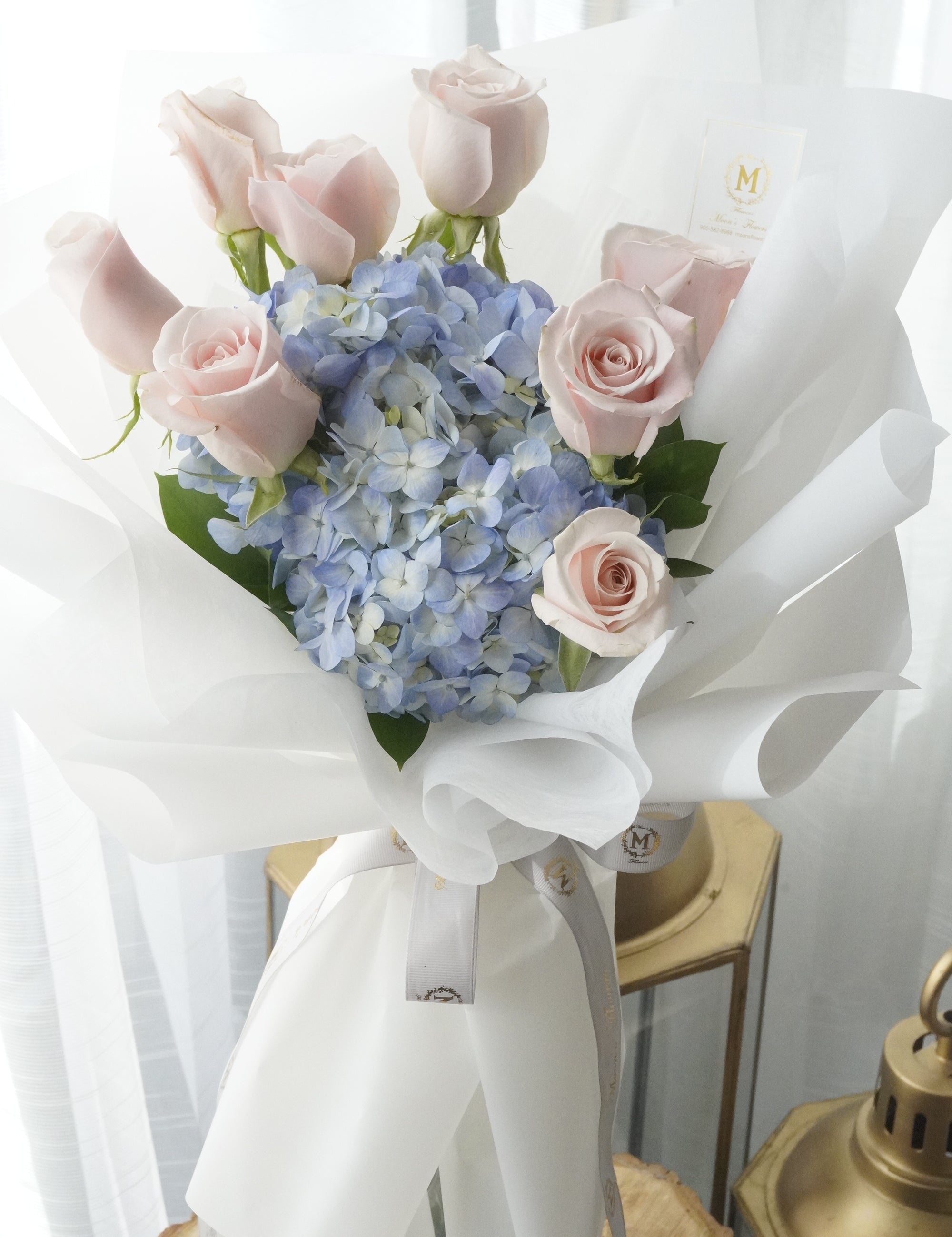 Cloud Daydream bouquet featuring blush pink roses and blue hydrangeas, wrapped in elegant white paper
