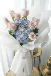 Cloud Daydream bouquet featuring blush pink roses and blue hydrangeas, wrapped in elegant white paper