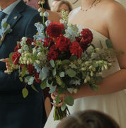 Bride and groom at wedding ceremony with red and blue floral bouquet featuring dahlias, hydrangeas, roses, and eucalyptus greenery — handcrafted bridal flowers by Moon's Flowers Toronto