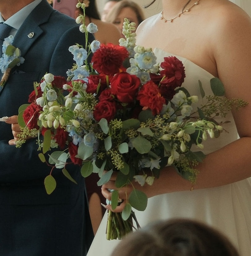 Bride and groom at wedding ceremony with red and blue floral bouquet featuring dahlias, hydrangeas, roses, and eucalyptus greenery — handcrafted bridal flowers by Moon's Flowers Toronto