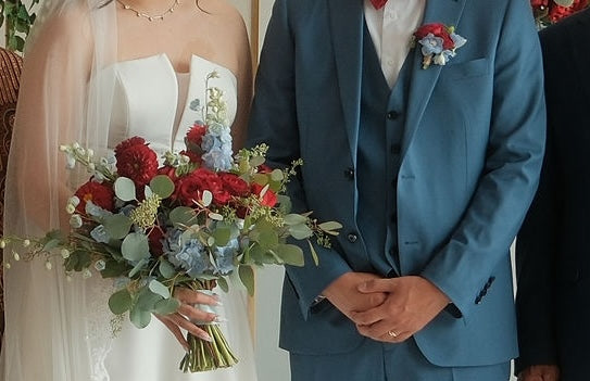 Bride holding a lush hand-tied bouquet of deep red roses, red dahlias, powder blue delphiniums, white tulips, and eucalyptus — Red & Blue Romance Bridal Bouquet by Moon's Flowers Toronto