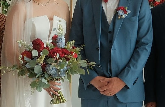 Bride holding a lush hand-tied bouquet of deep red roses, red dahlias, powder blue delphiniums, white tulips, and eucalyptus — Red & Blue Romance Bridal Bouquet by Moon's Flowers Toronto