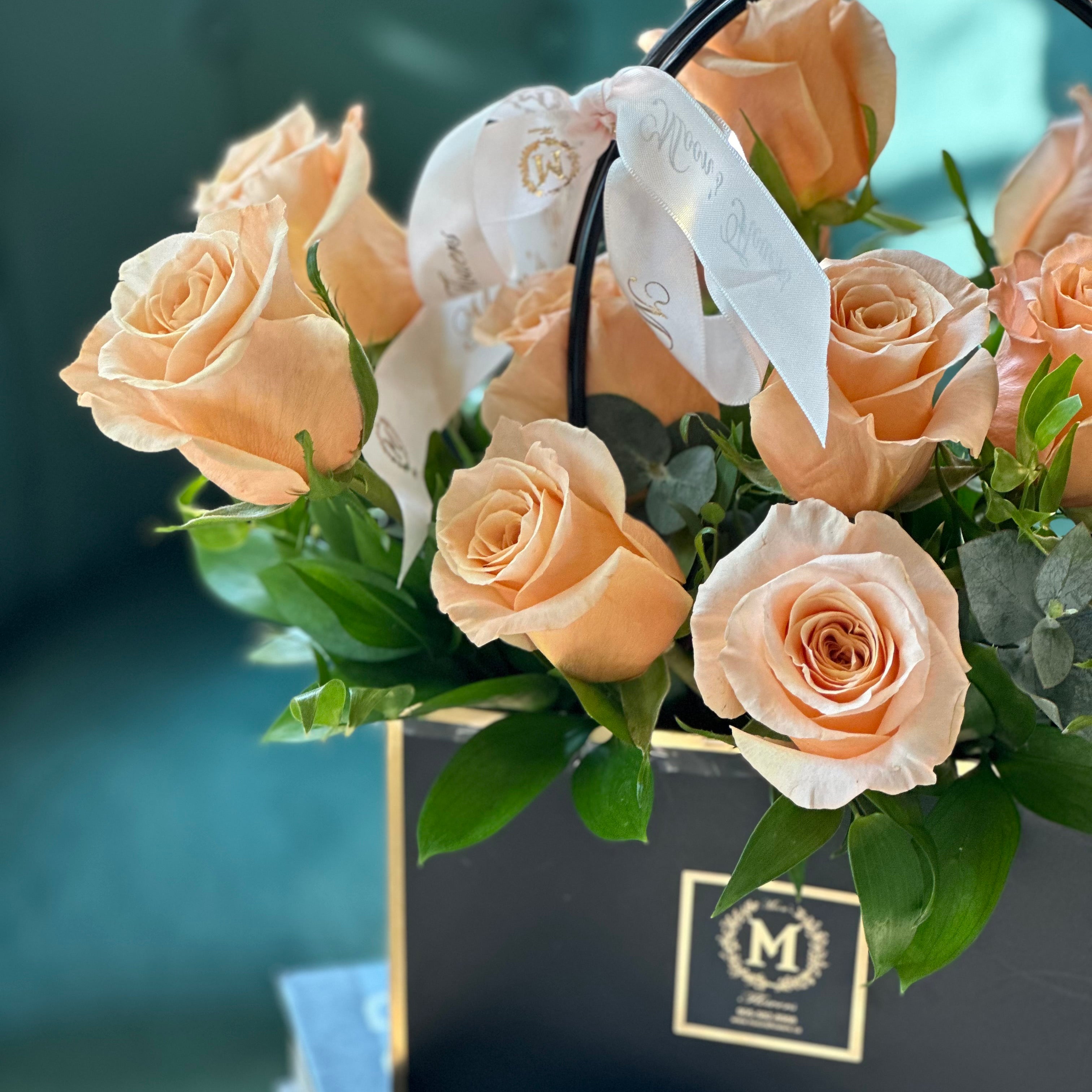 Close-up of peach roses and eucalyptus in the Dozen Peach Roses – Basket of Love arrangement
