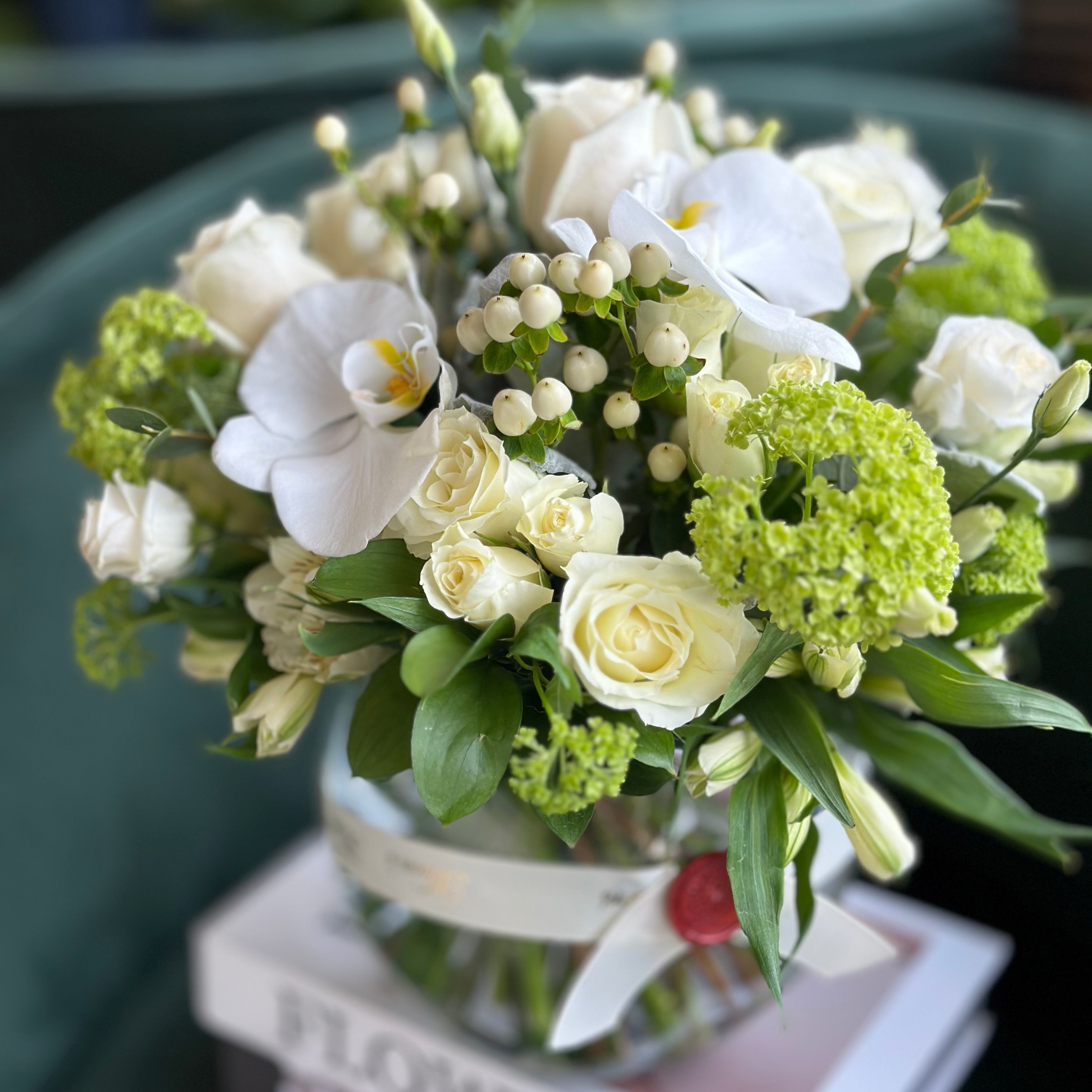 Elegant Mother's Day flower arrangement featuring white orchids, ivory roses, and green hydrangeas in a glass vase. A premium 'Designer's Choice' bouquet for same-day delivery in Toronto