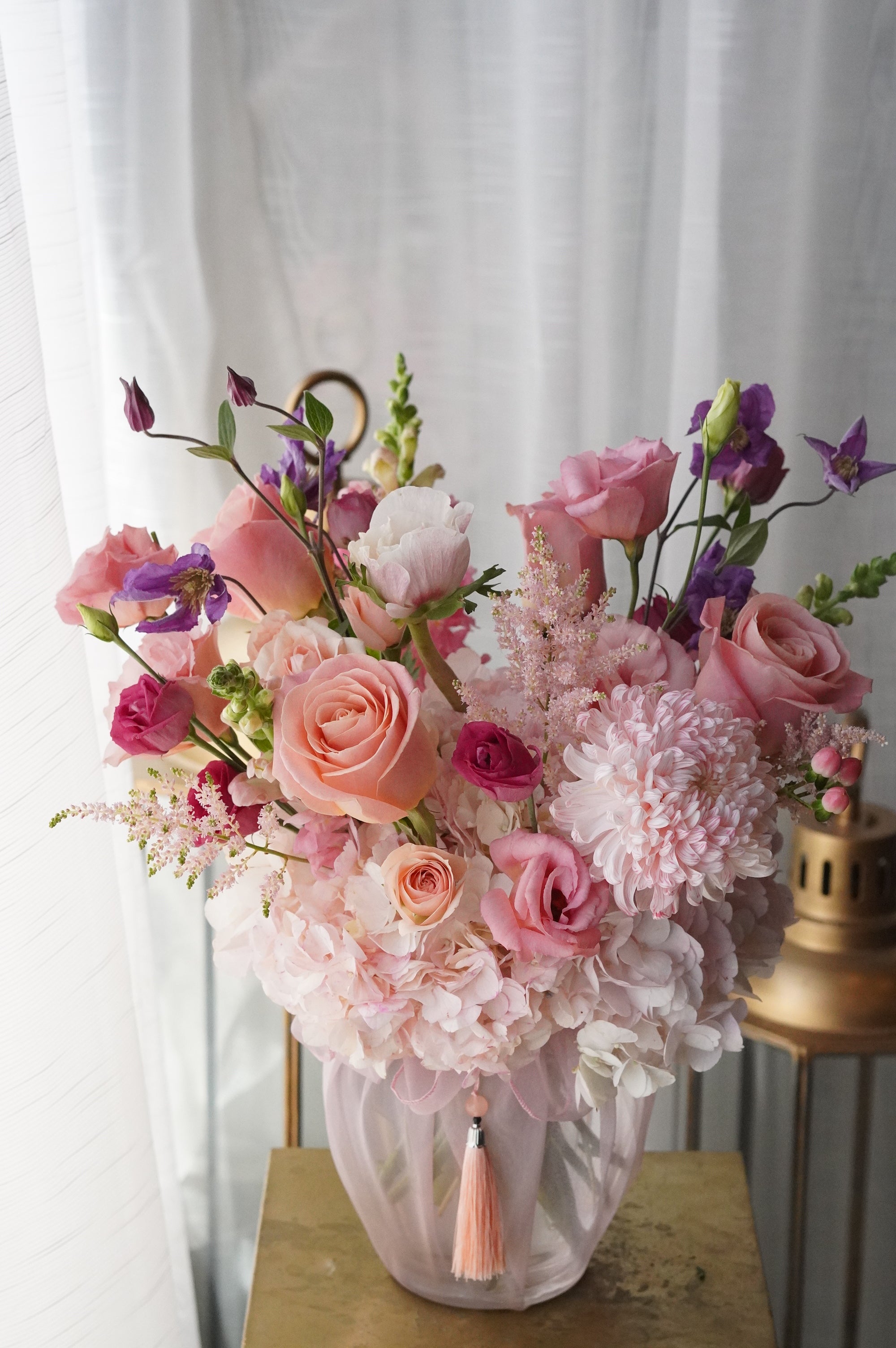 Elegant Mother's Day flower arrangement in a glass vase featuring pink peonies, peach roses, and purple campanula with a decorative silk tassel. Professional florist delivery in Toronto and Oakville