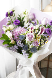 Elegant Purple Rush Mother's Day bouquet featuring lavender roses, purple calla lilies, and blue thistles in a white designer wrap. Luxury hand-tied floral gift by Moon's Flowers, available for same-day delivery in Toronto