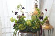 Elegant wedding centerpiece featuring deep burgundy roses, red ranunculus, and lush greenery in a glass vase