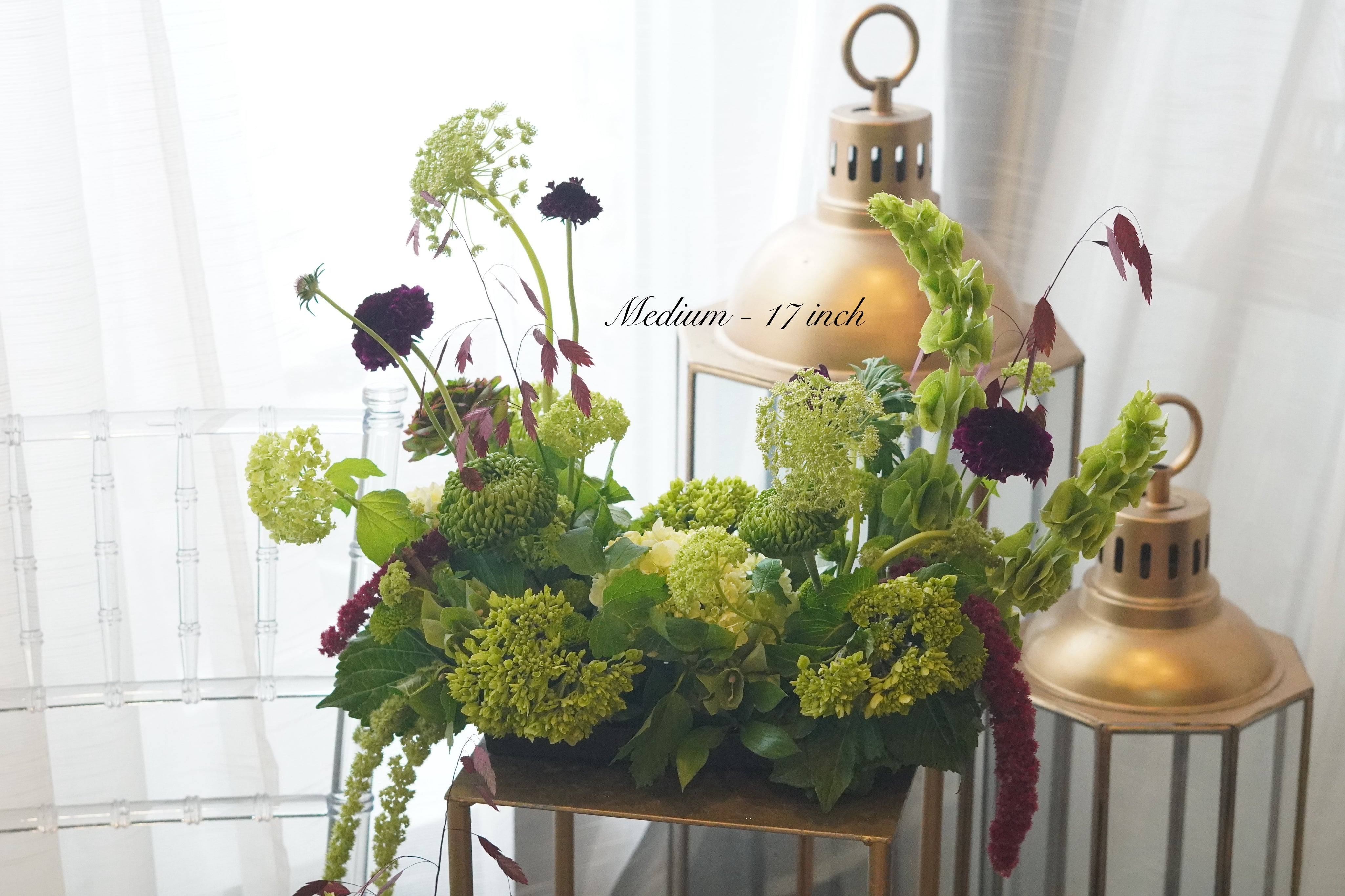 Elegant wedding centerpiece featuring deep burgundy roses, red ranunculus, and lush greenery in a glass vase